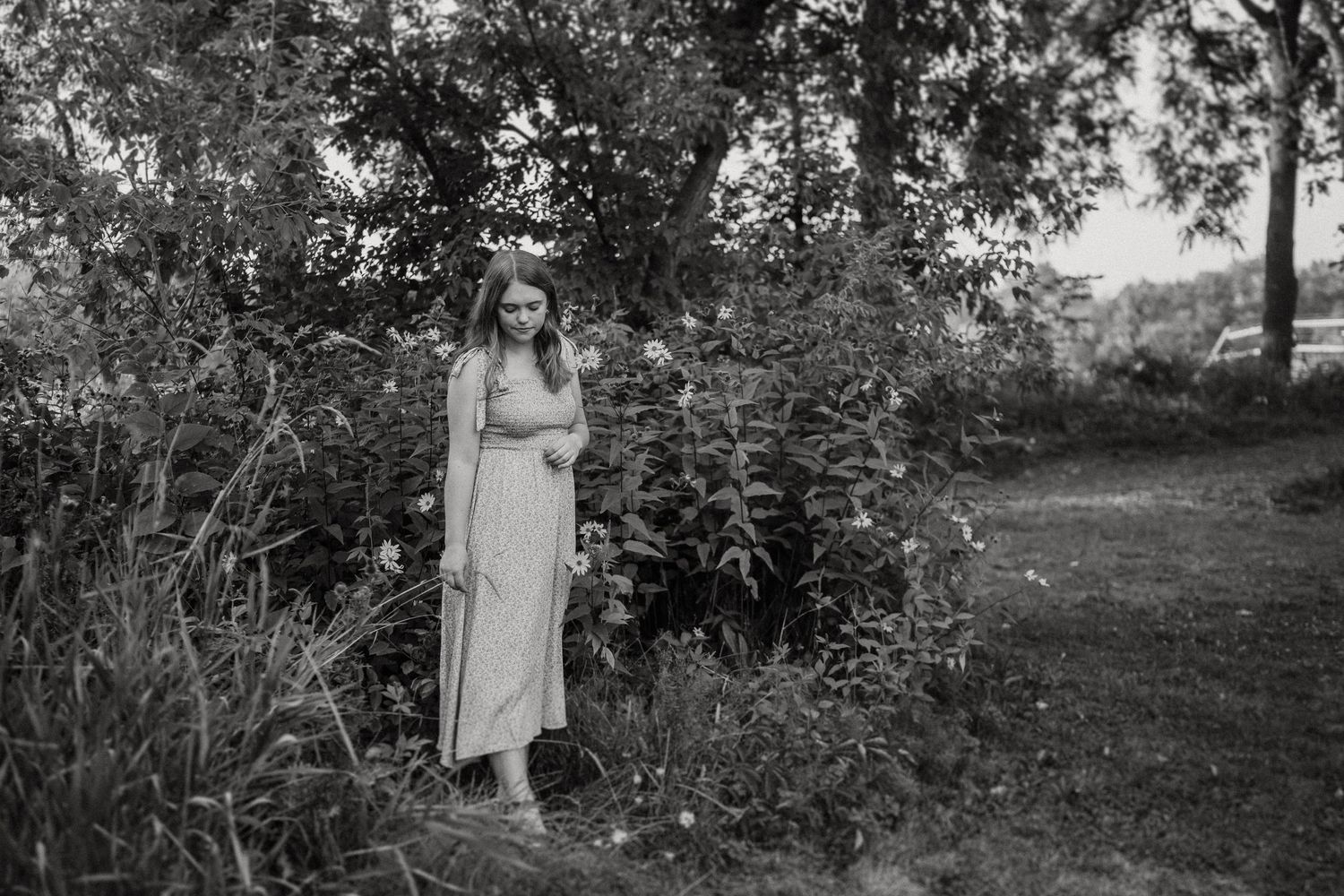 Black and white image of someone in a flowing dress standing in a wild garden setting.