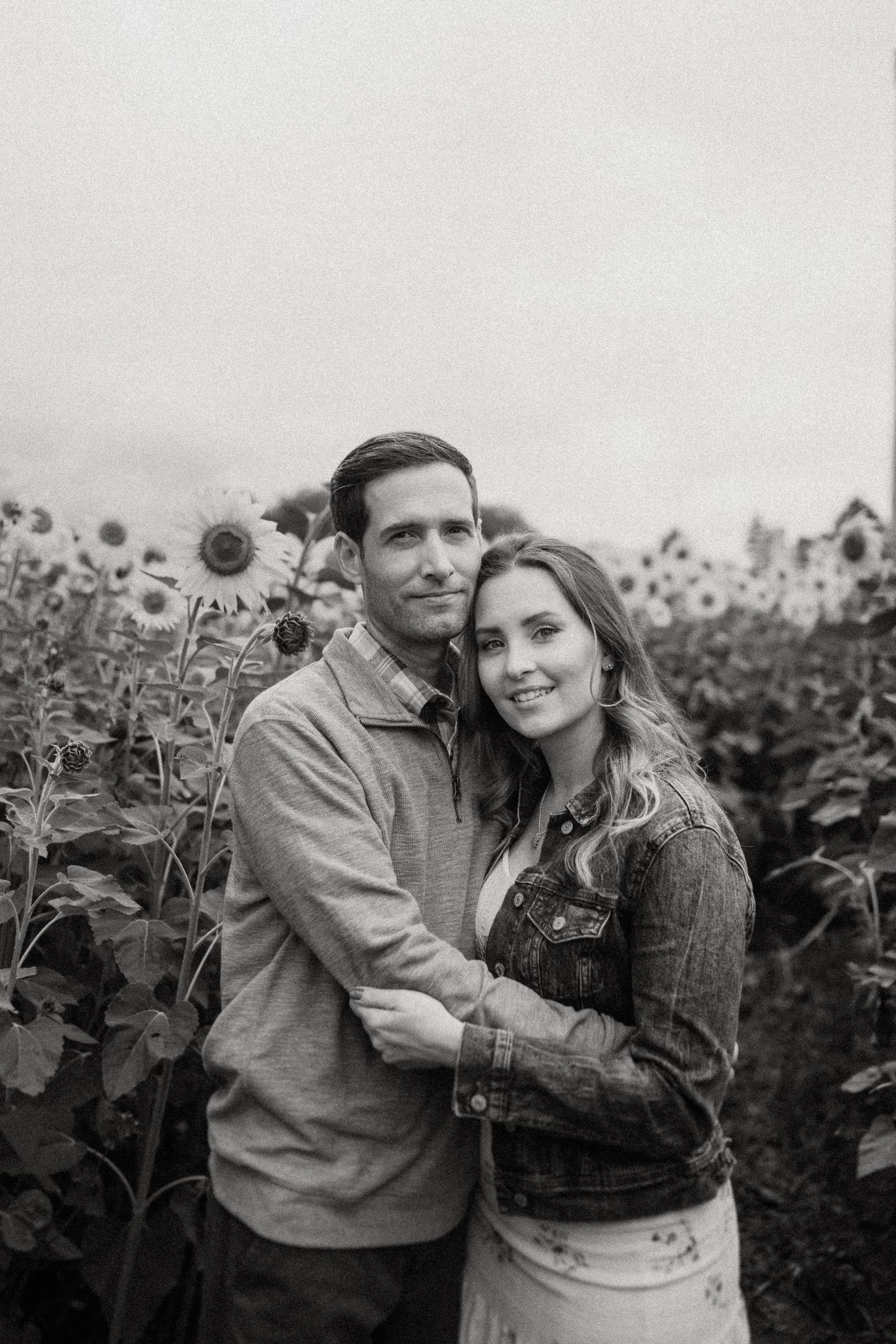 A black and white portrait of a couple embracing in a sunflower field.