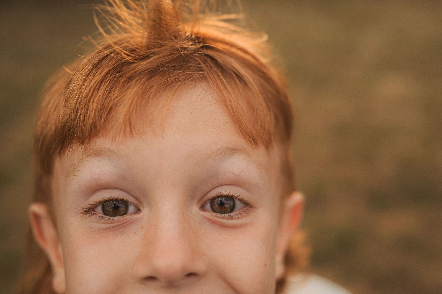 Close up of child's eyes and forehead against blurred brown background.