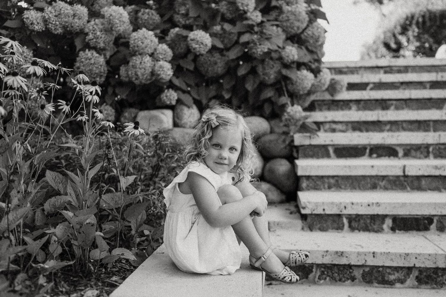 Black and white garden photo on stone steps surrounded by flowering shrubs and rocks.