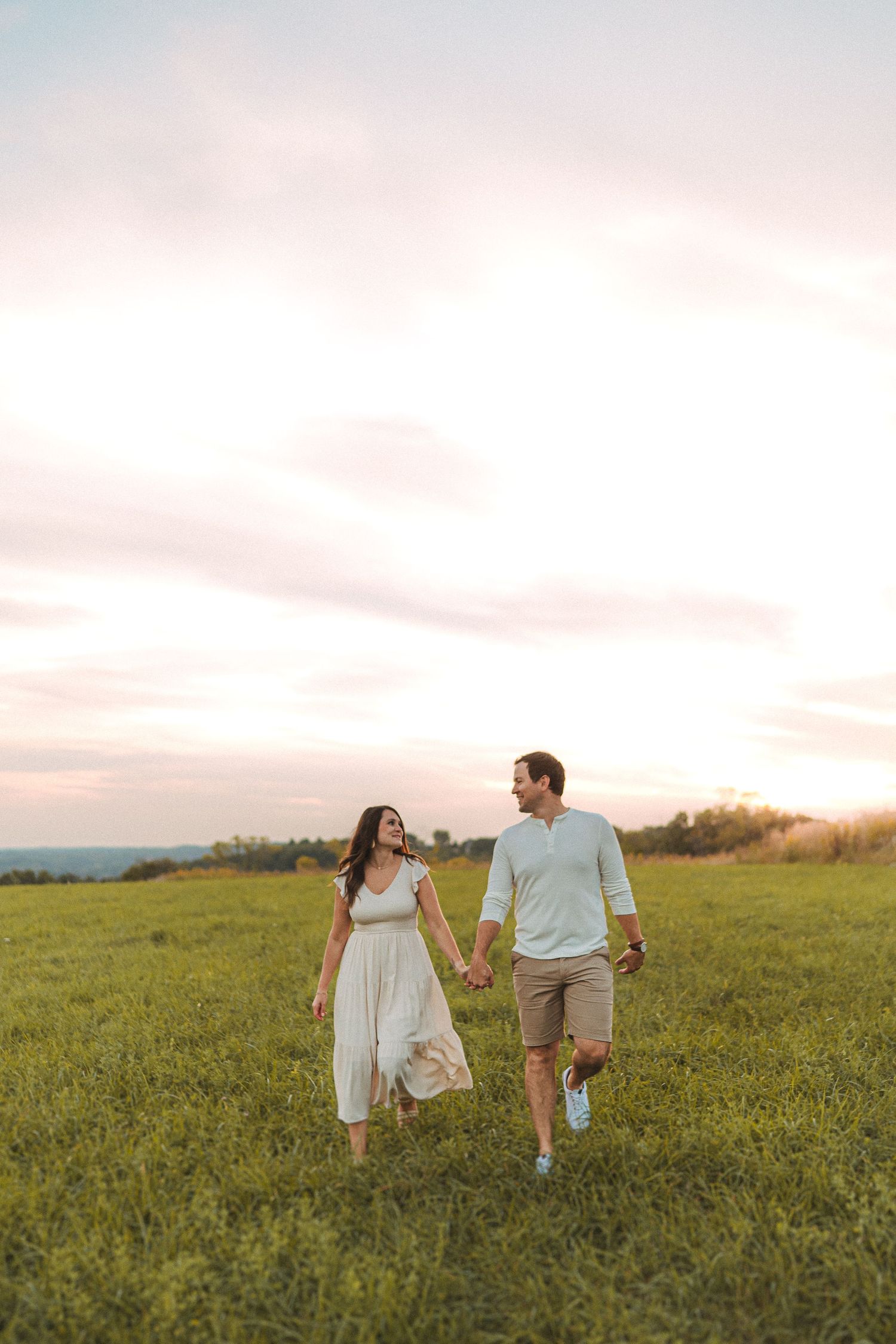 Couple walks through sunlit meadow holding hands during golden hour.