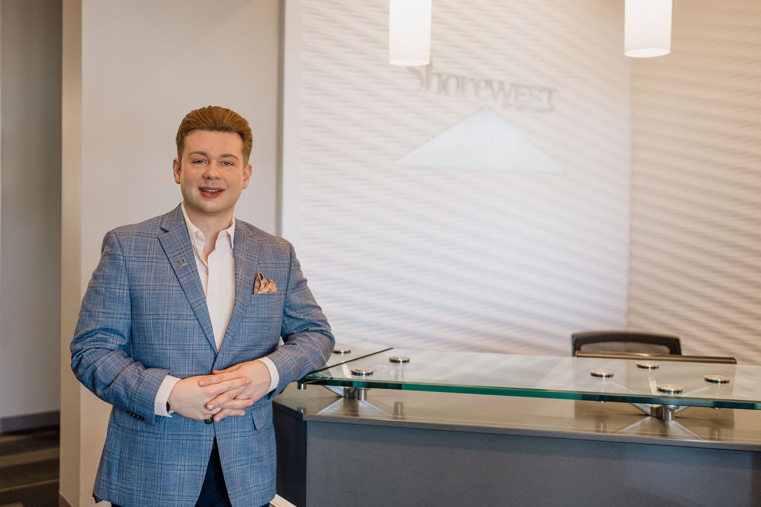Professional in blue plaid blazer and pocket square stands in modern office reception area.