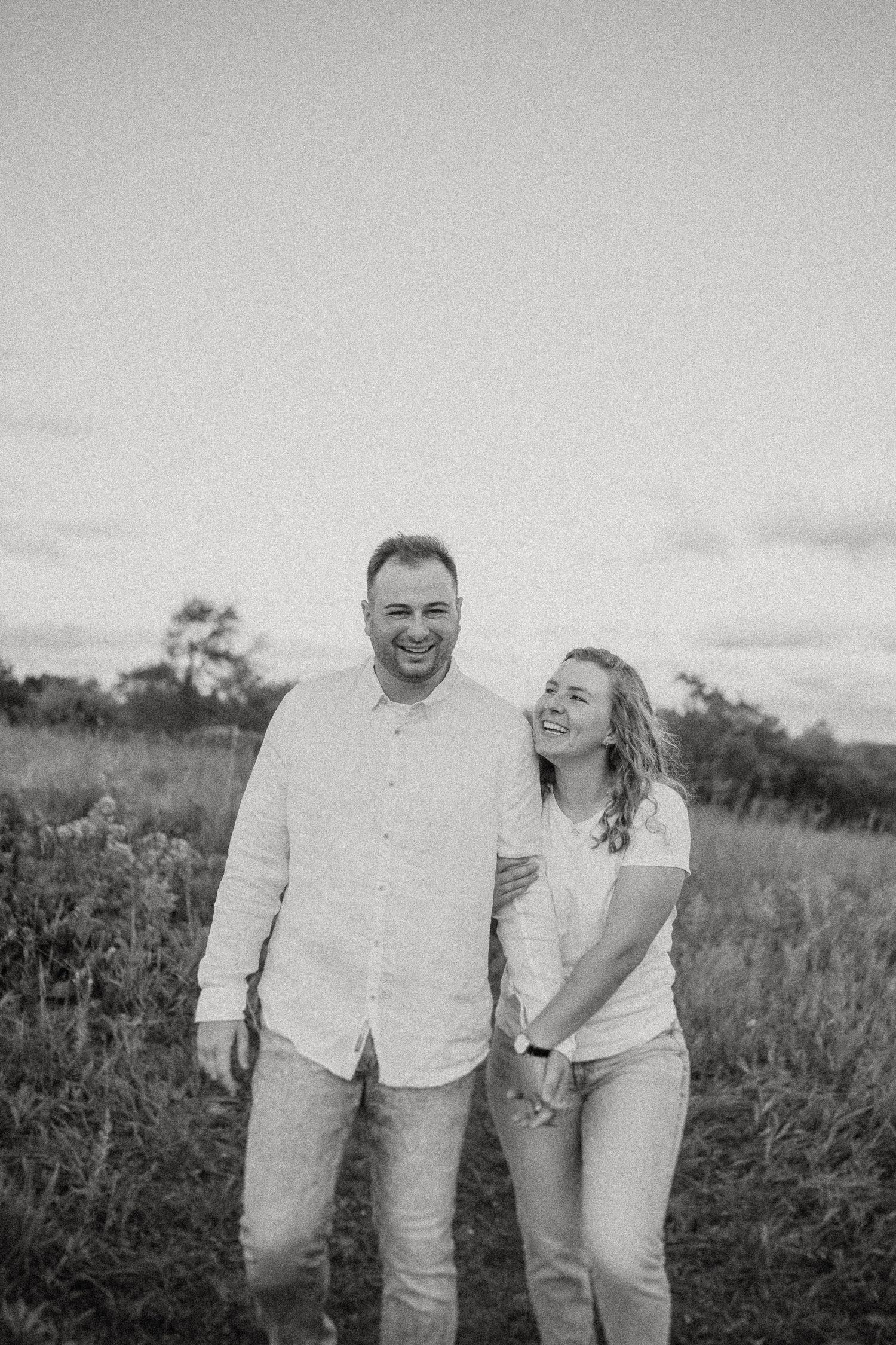 A black and white portrait of a couple sharing genuine laughter in an outdoor field setting.