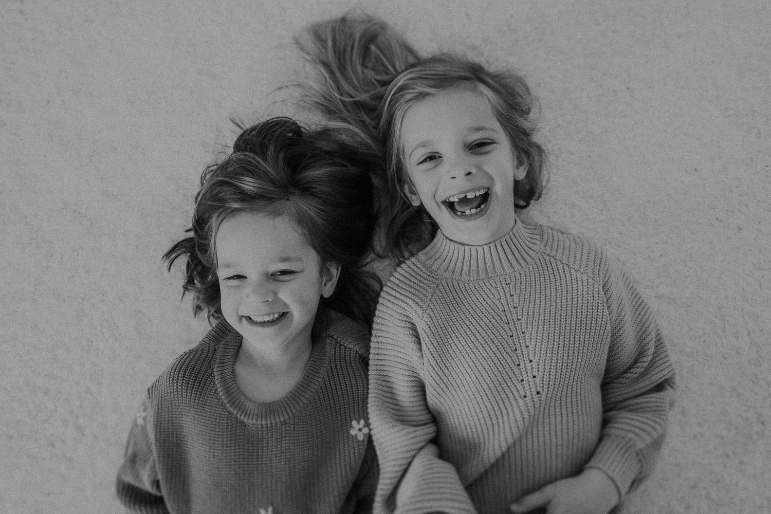 A candid black and white portrait shows two people laughing in matching knit sweaters.