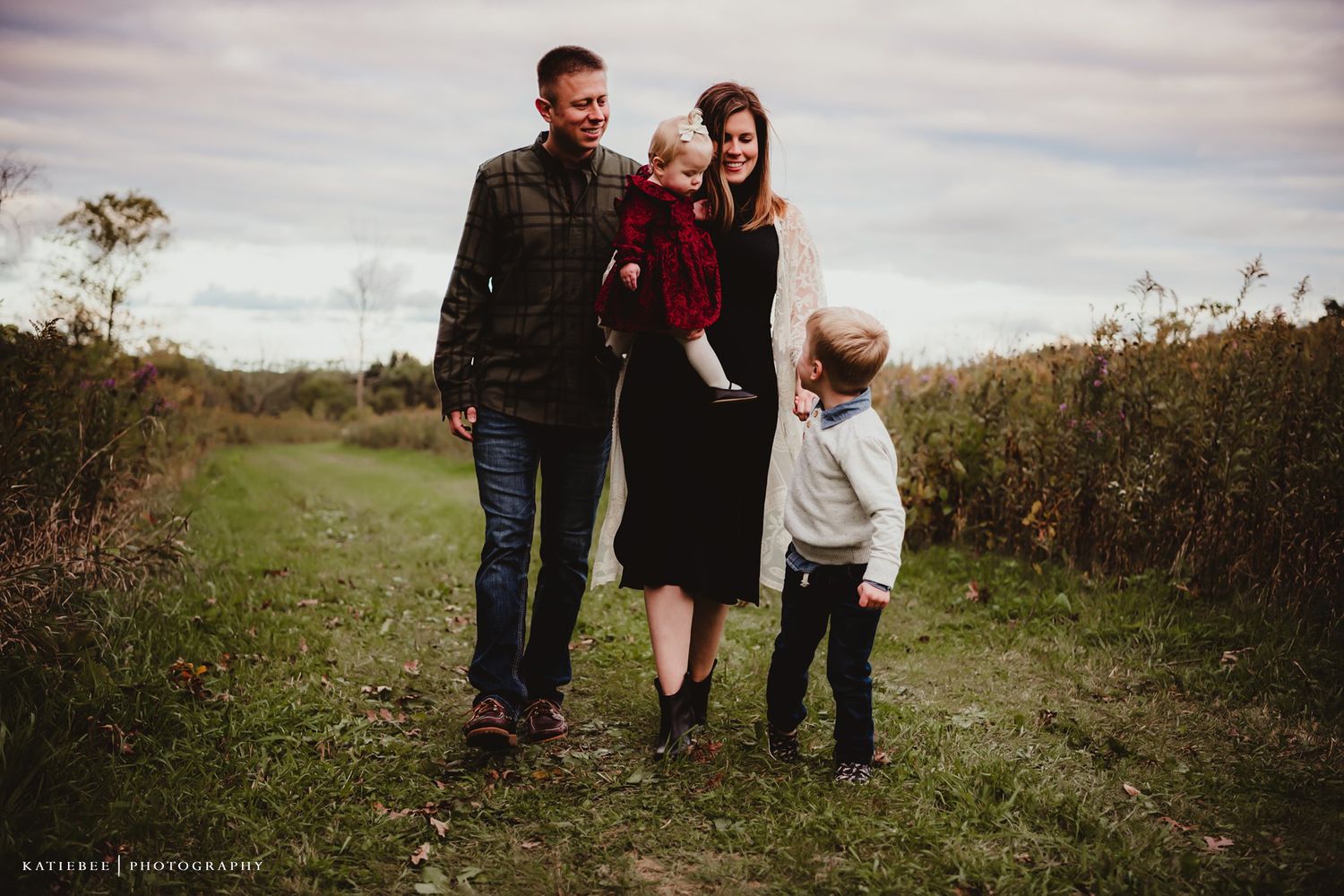 Family walking together on rustic dirt path through autumn fields.