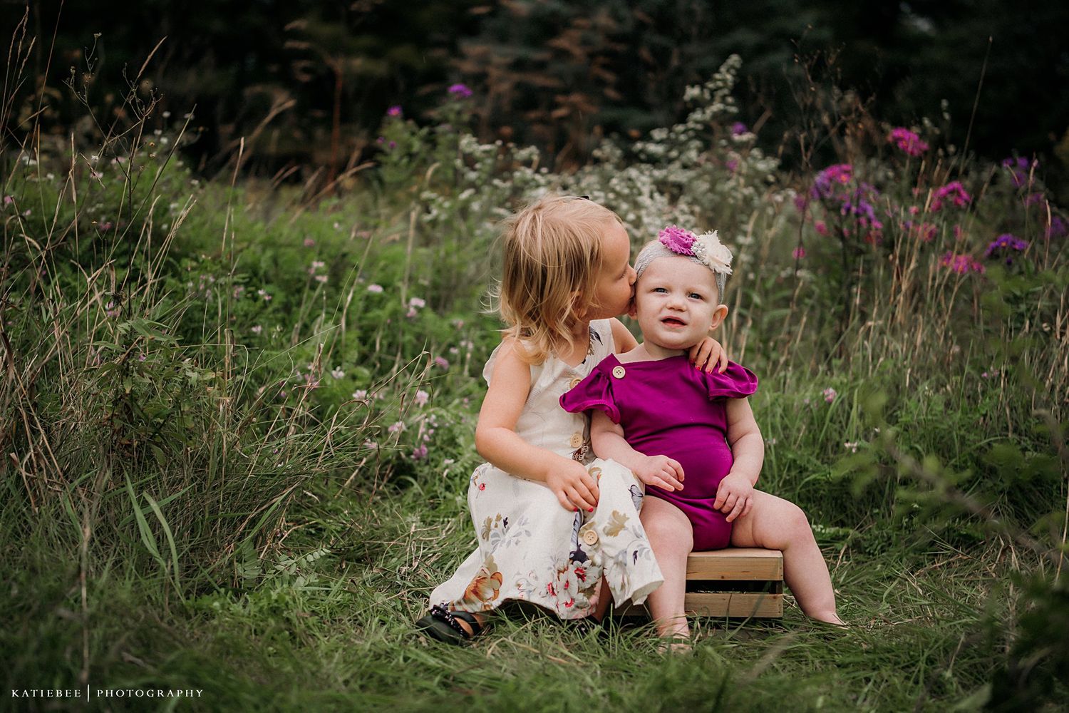 Two children share a sweet moment while sitting in a wildflower meadow.