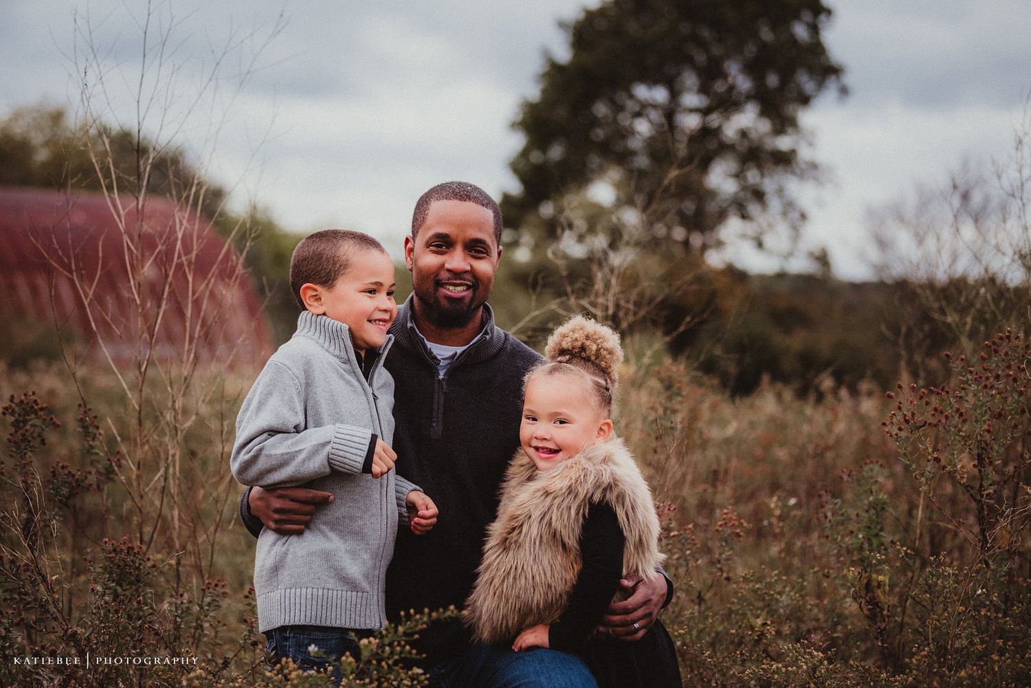 Family portrait captured in natural setting with fall foliage and golden hour lighting.