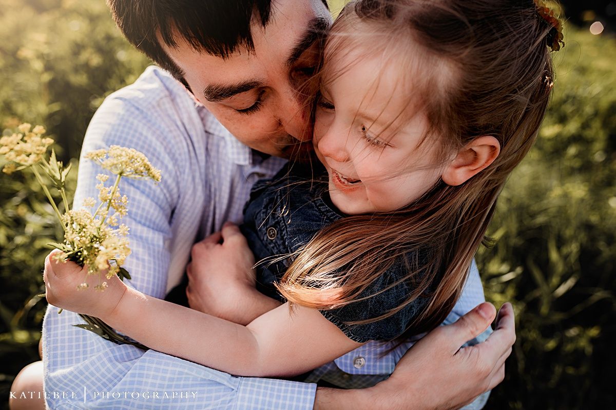 Intimate embrace captured in a golden field during sunset with soft natural lighting.