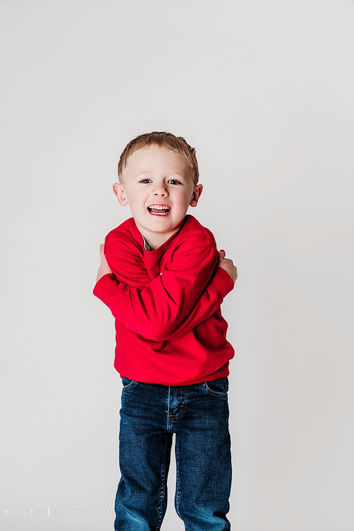 Joyful child in red sweater and jeans posing against white background.