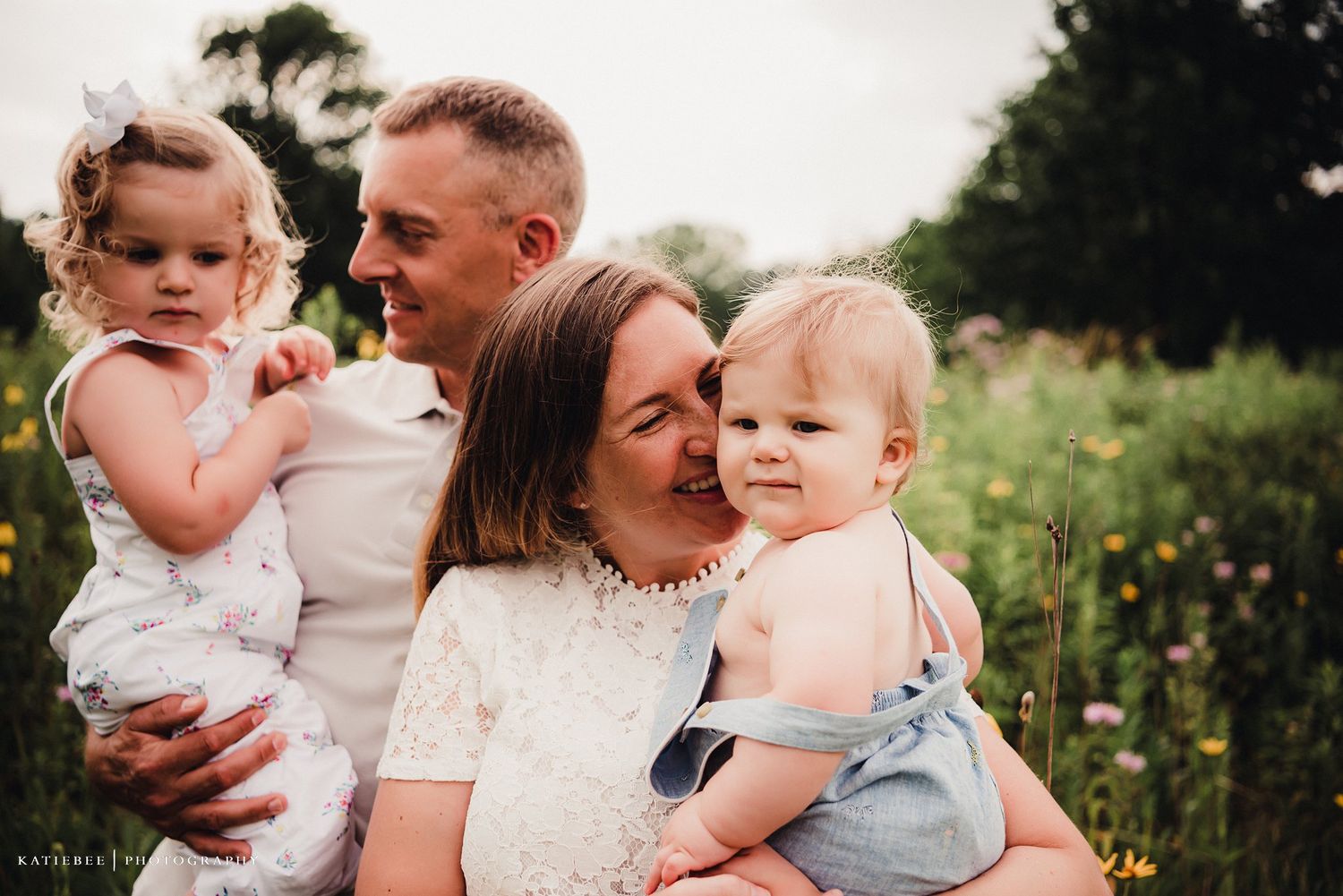 A loving family moment captured outdoors in a wildflower meadow during golden hour.