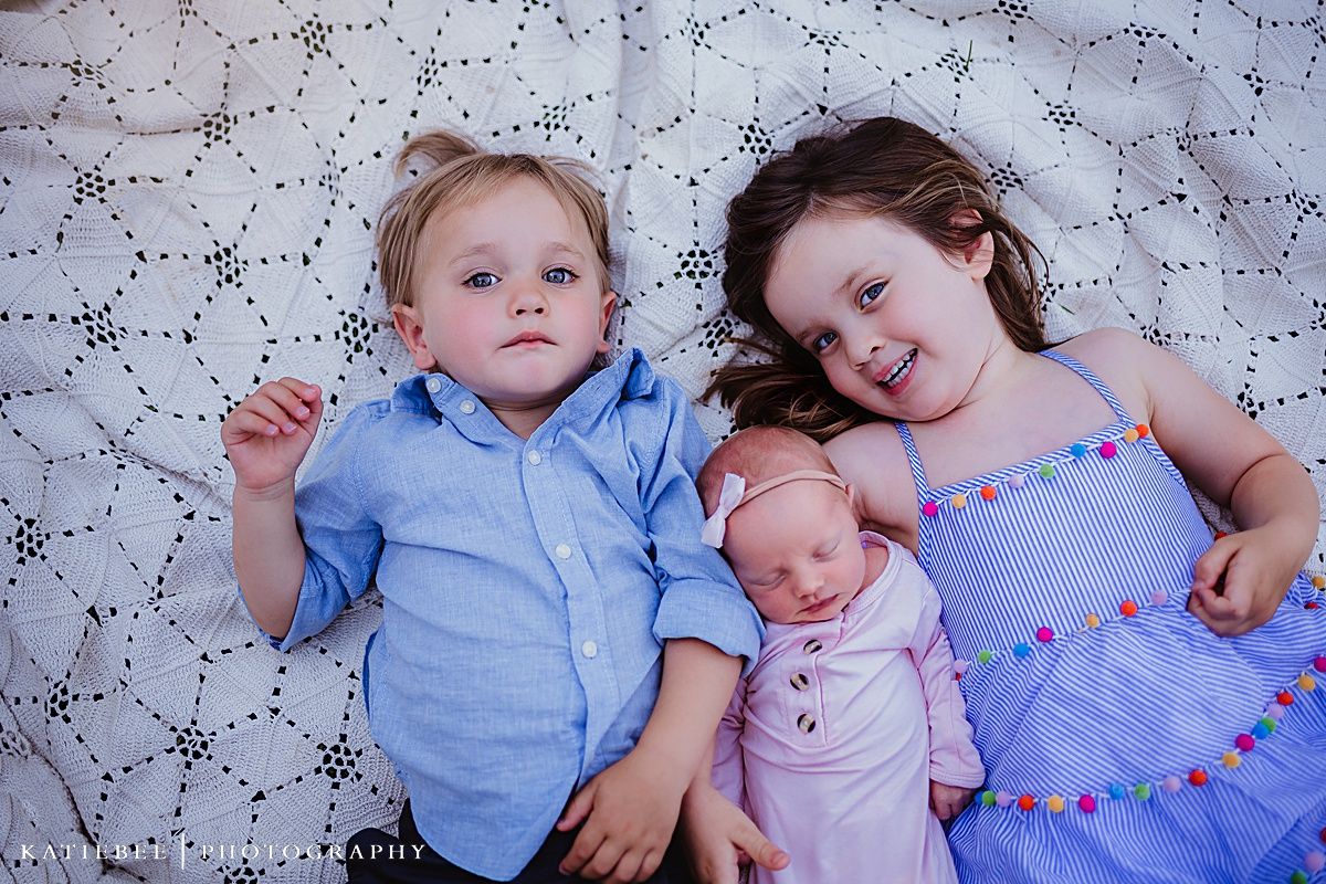 Young siblings resting together on a patterned blanket in coordinated blue and pink outfits.