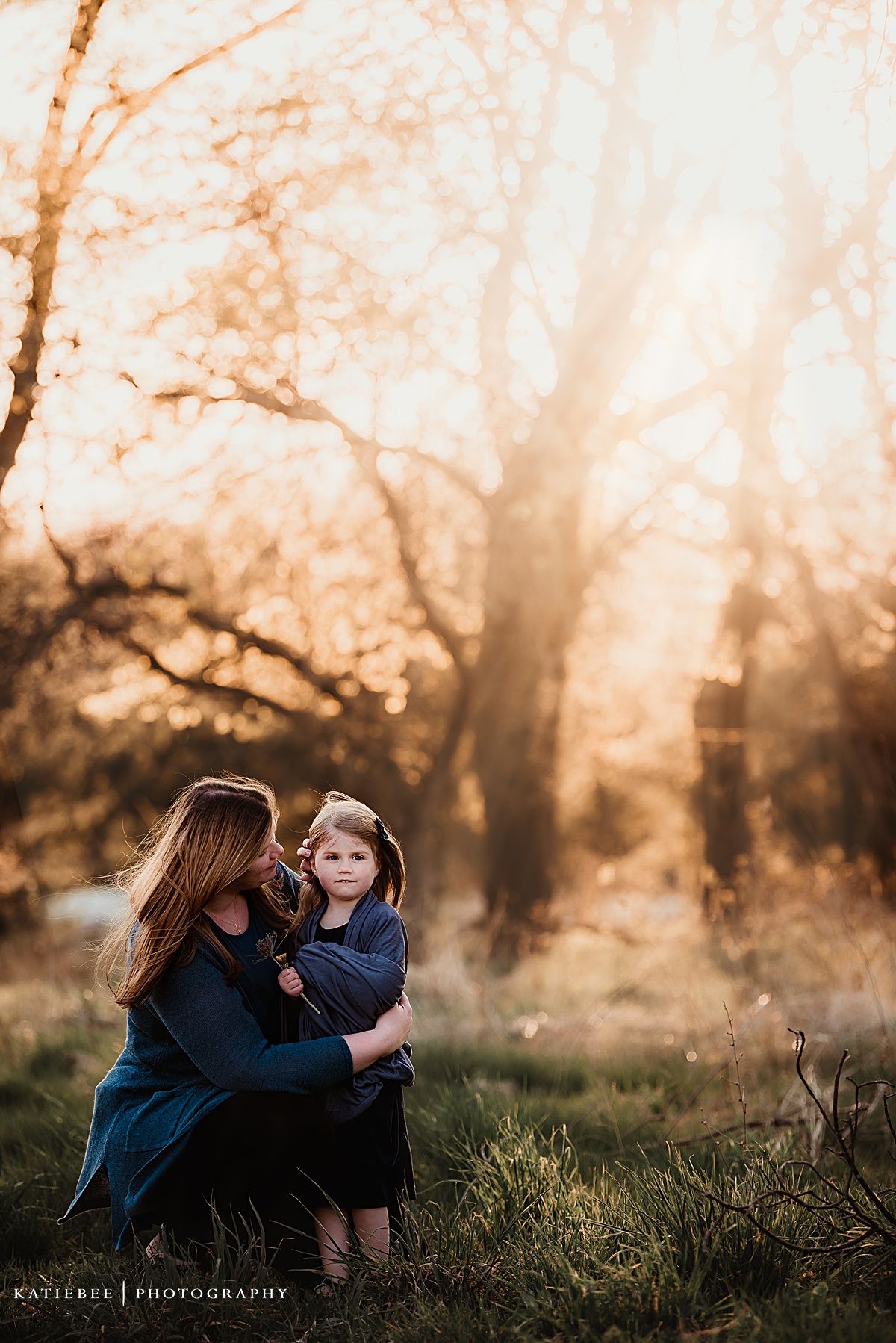 Sweet lifestyle portrait of parent and child sitting in golden sunset grass.