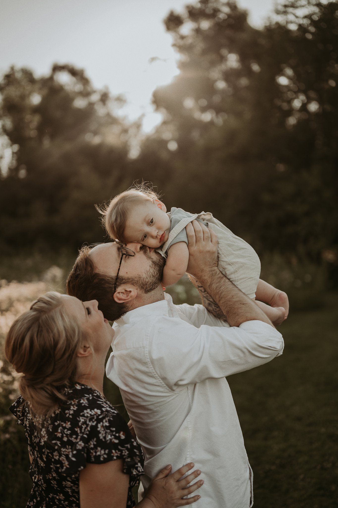 Intimate family moment outdoors as child is lifted up for kisses at sunset.