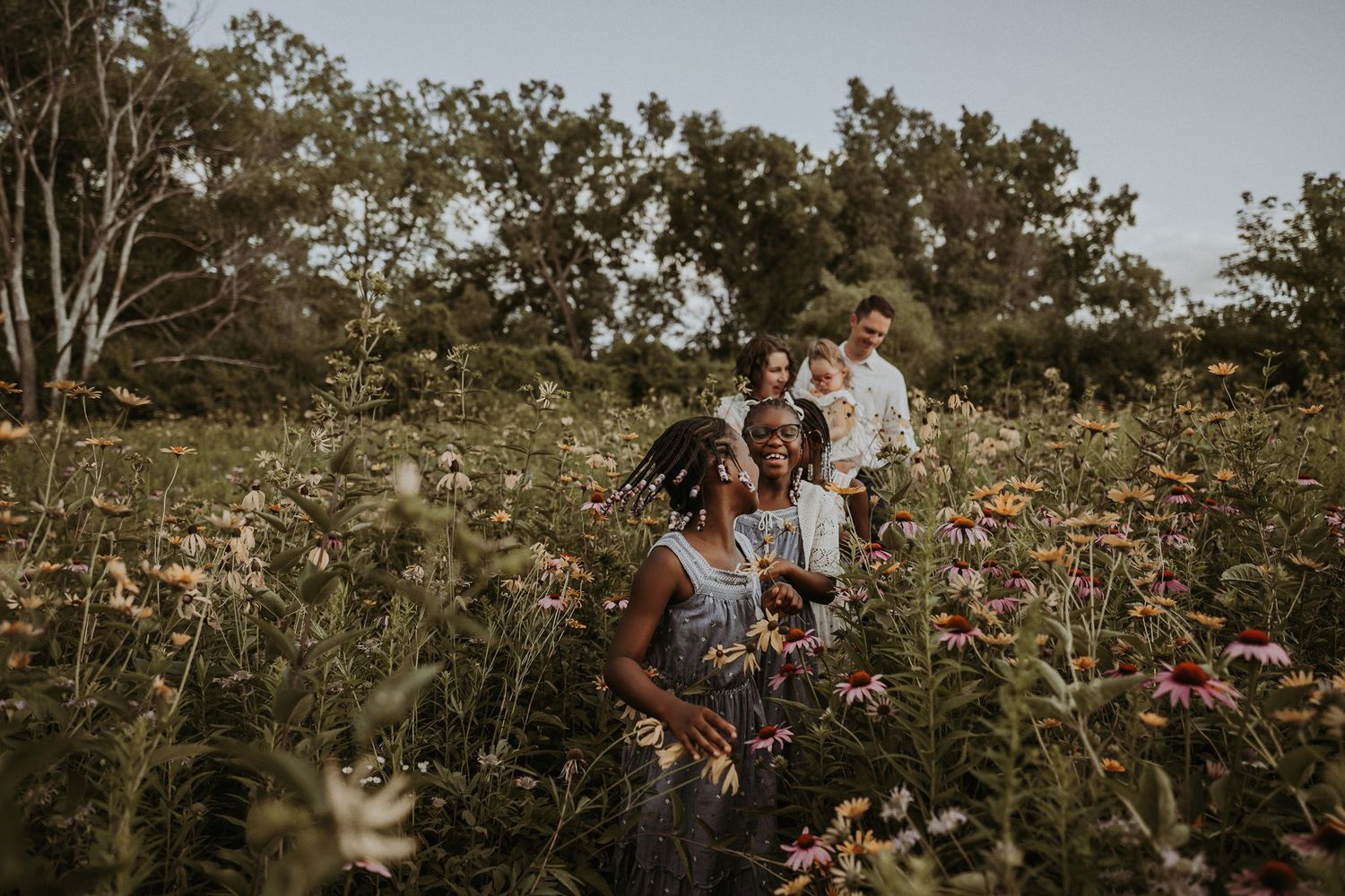 A group gathers in a field of wildflowers during golden hour surrounded by trees.