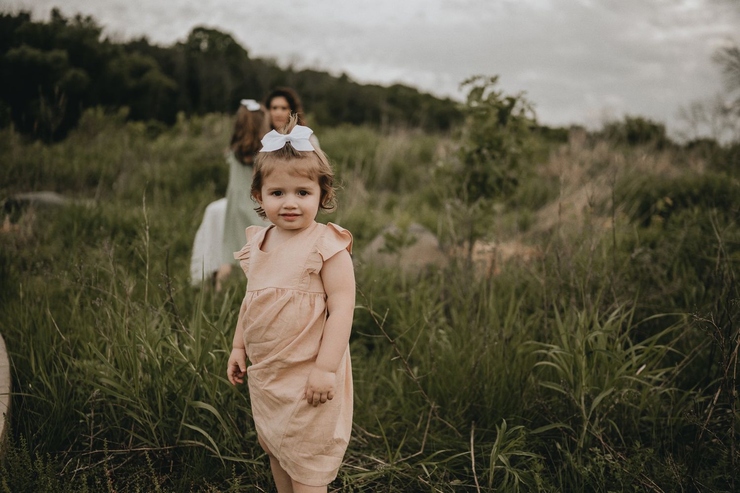 A candid moment of a child in peachy-pink attire running through tall grass during golden hour.