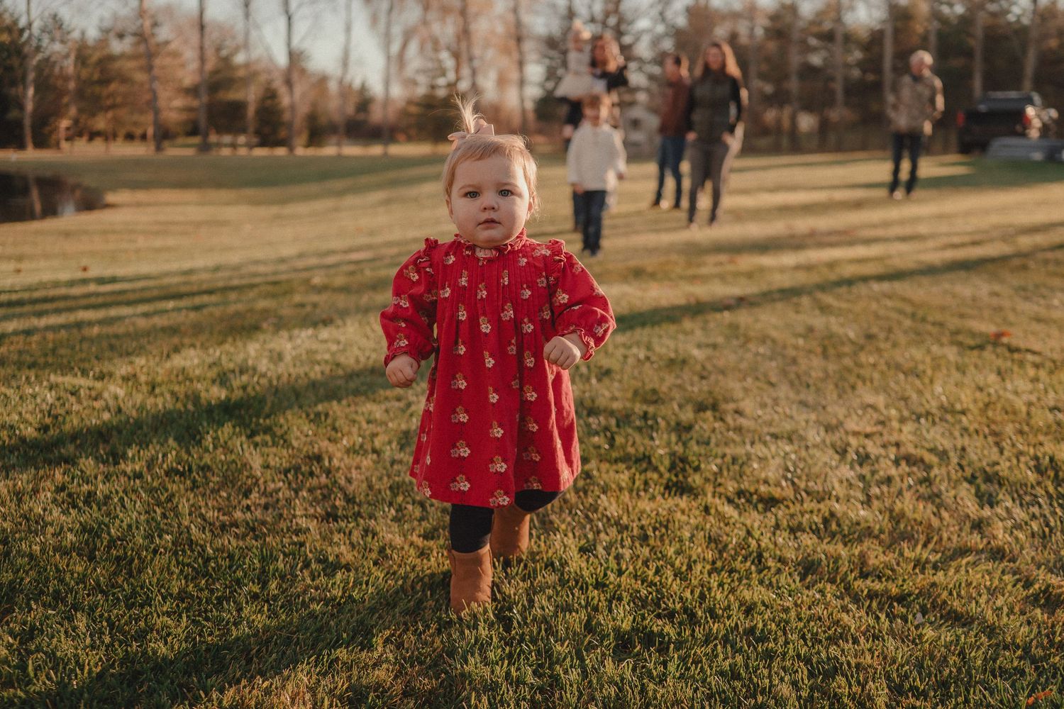 A small child in a red dress walks through a grassy field during golden hour.