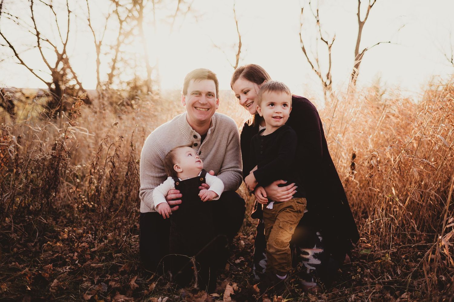 Family posing together in a golden autumn field at sunset.
