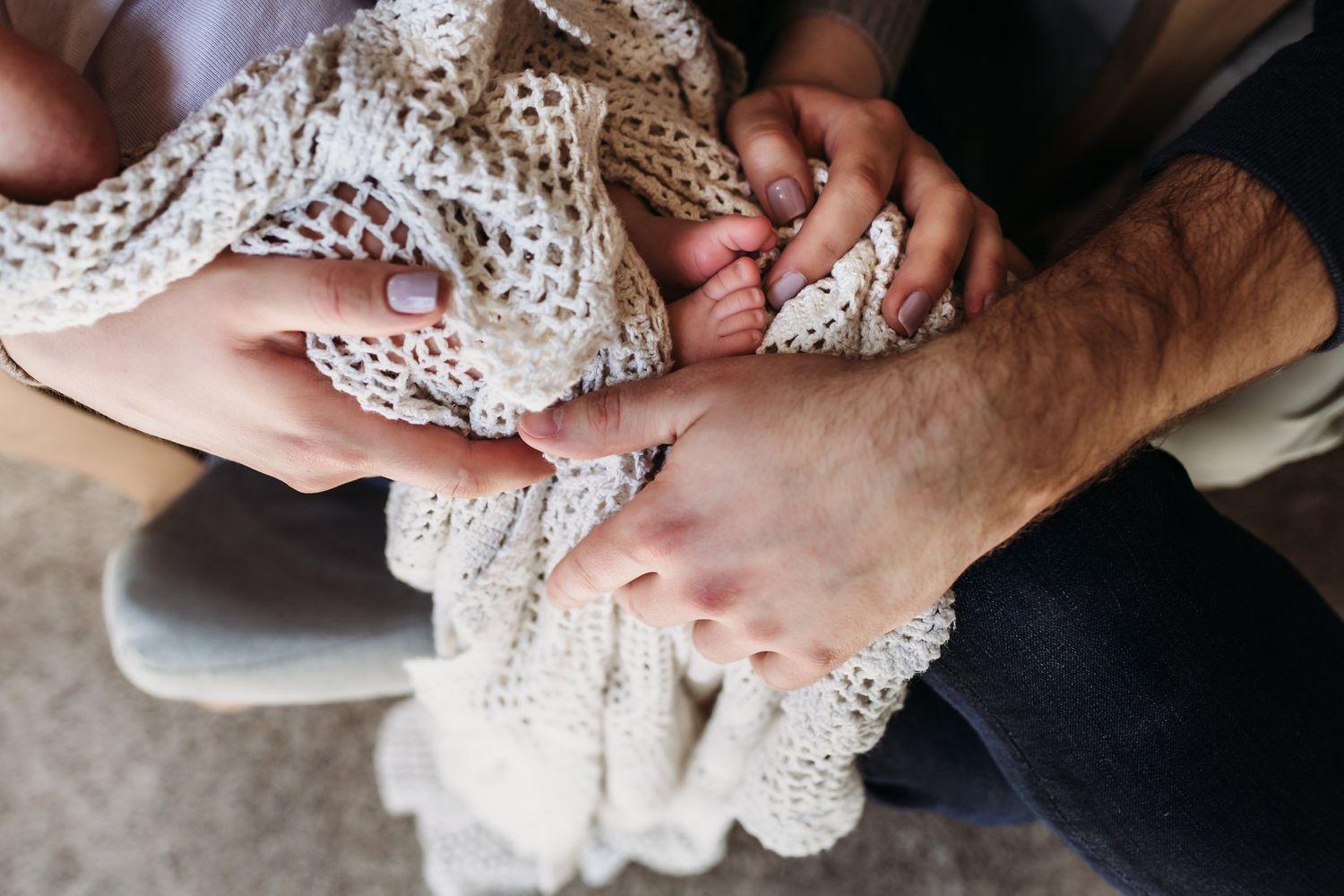 Close-up of hands holding delicate cream knit blanket with baby.