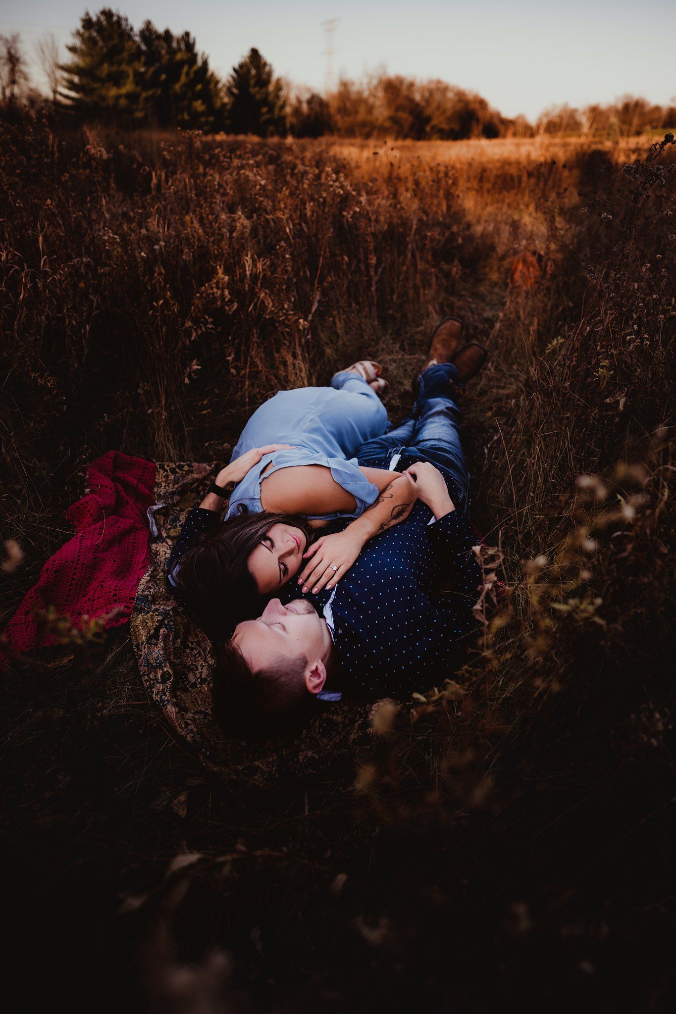 Couple lying in autumn field during sunset engagement photo session.