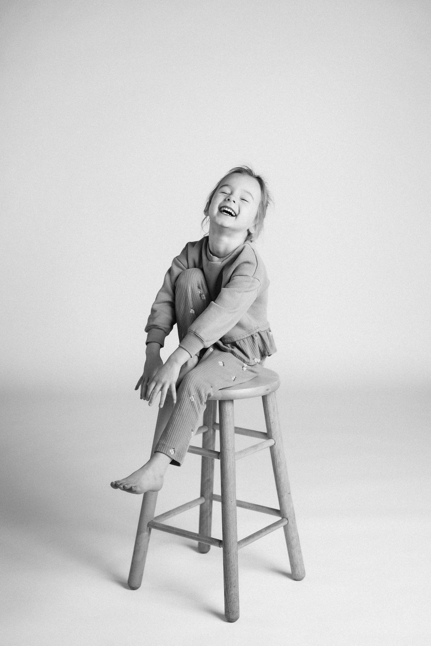Black and white photo series showing playful movements on a wooden stool against a white background.
