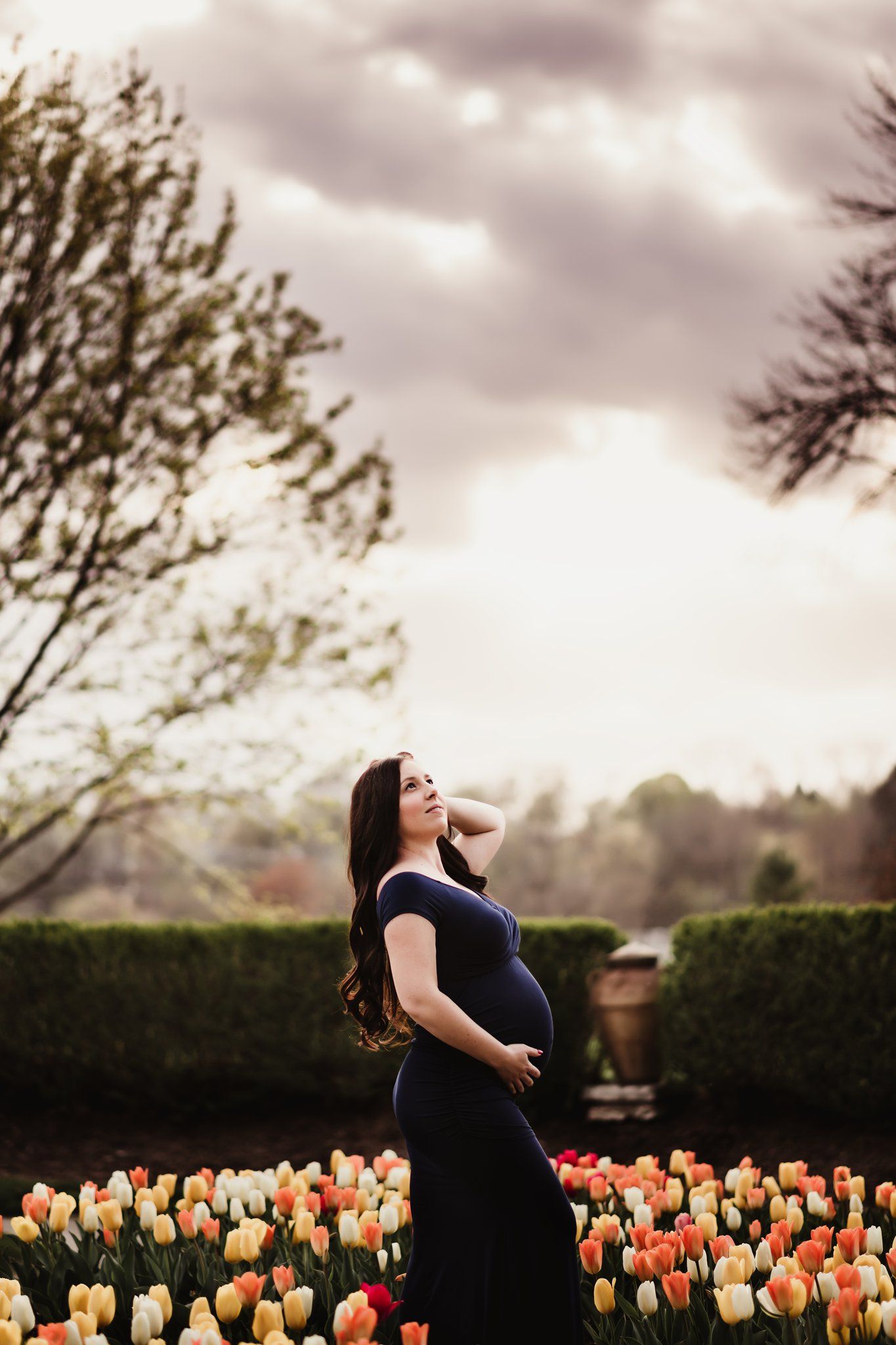 Woman in navy dress poses in garden with blooming orange and yellow tulips.