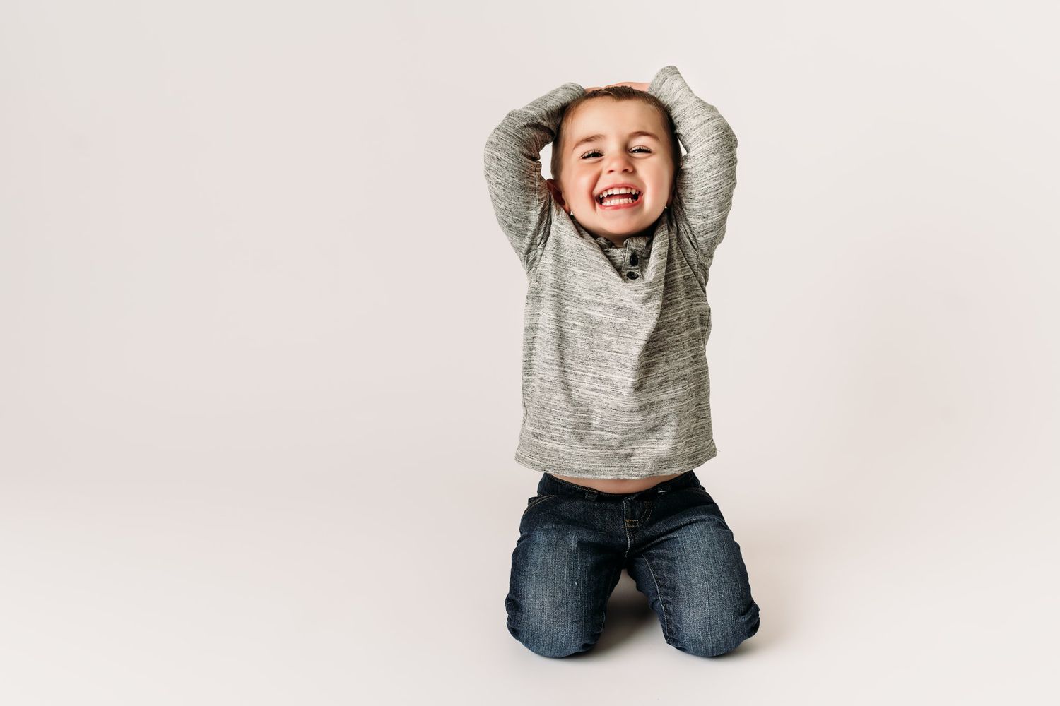 Energetic pose with hands raised above head while kneeling on white background.