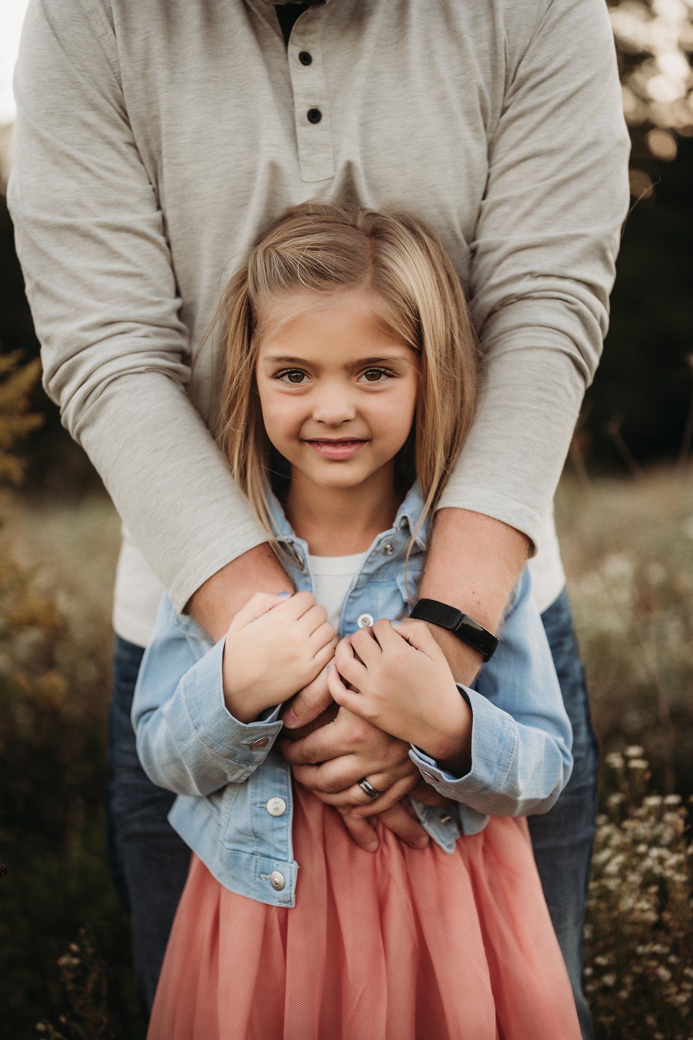 A sweet portrait showing a person holding a child wearing a pink dress and denim jacket outdoors.