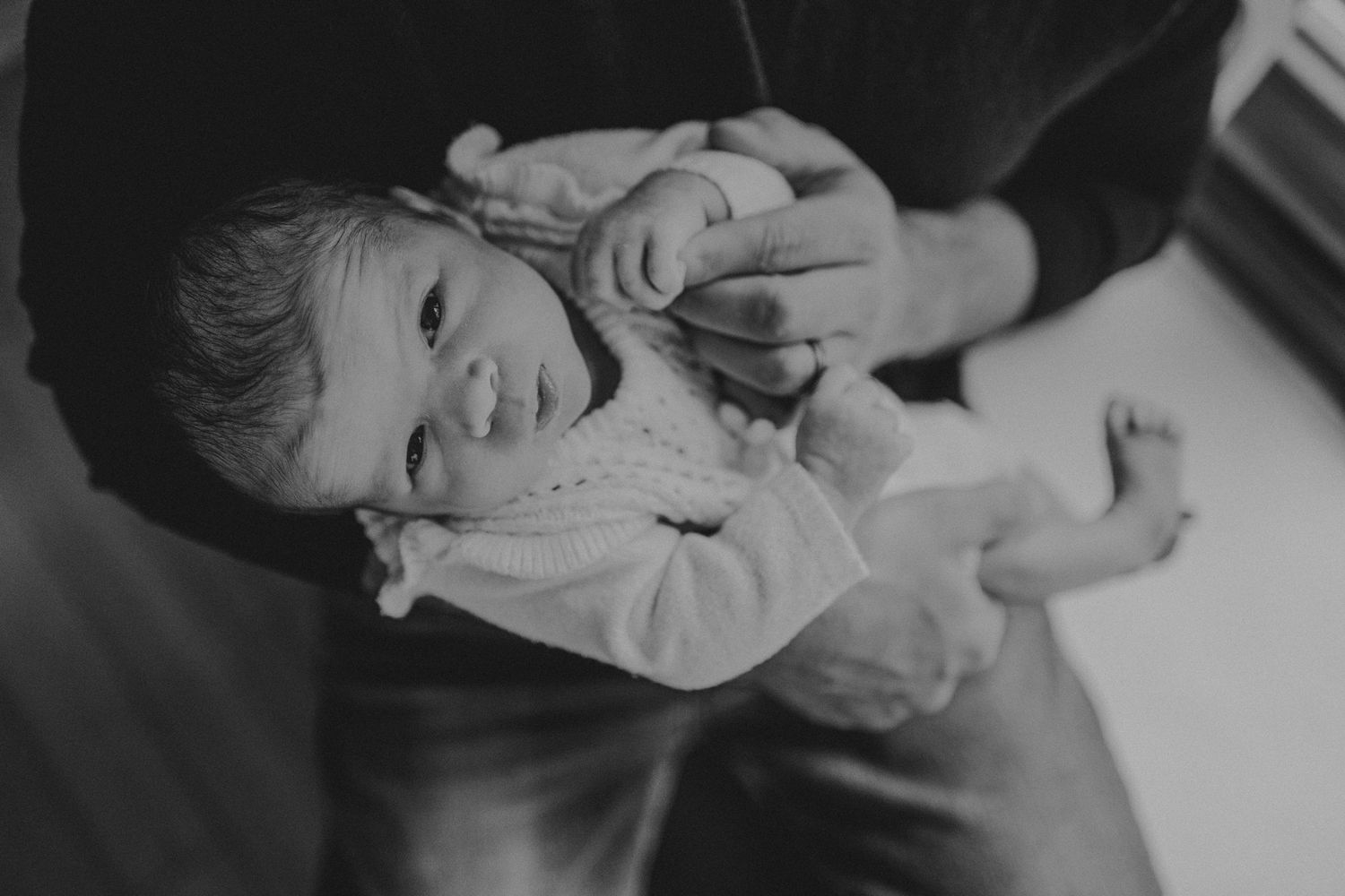 Black and white portrait of baby in white clothing looking up with expression of wonder.