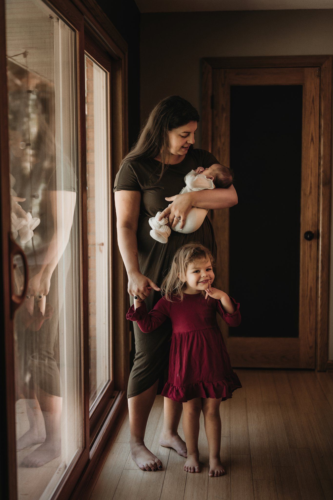Mother and children share a sweet moment by large windows in their home.