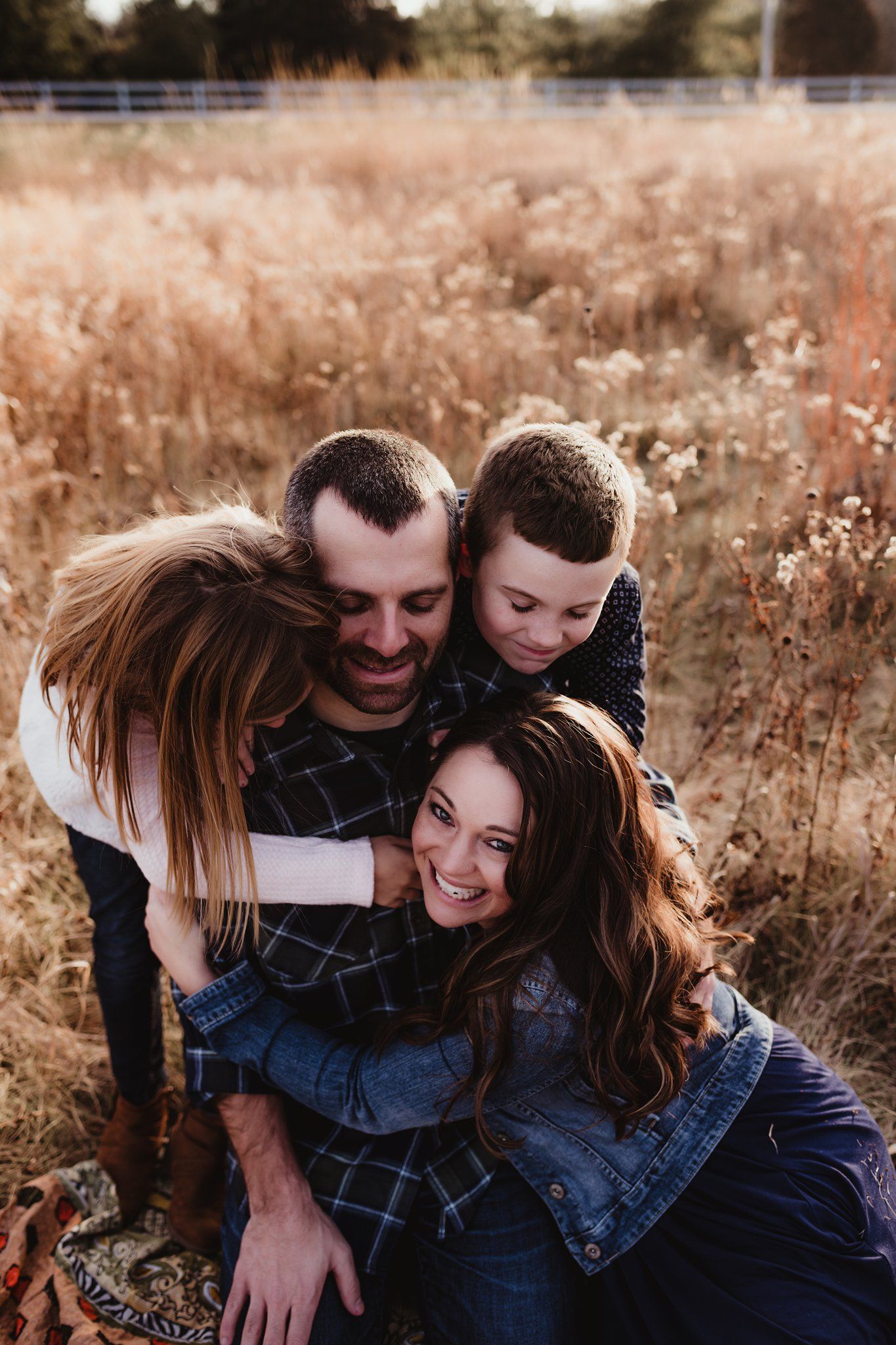 Family embracing and laughing together in field of golden grass at sunset.