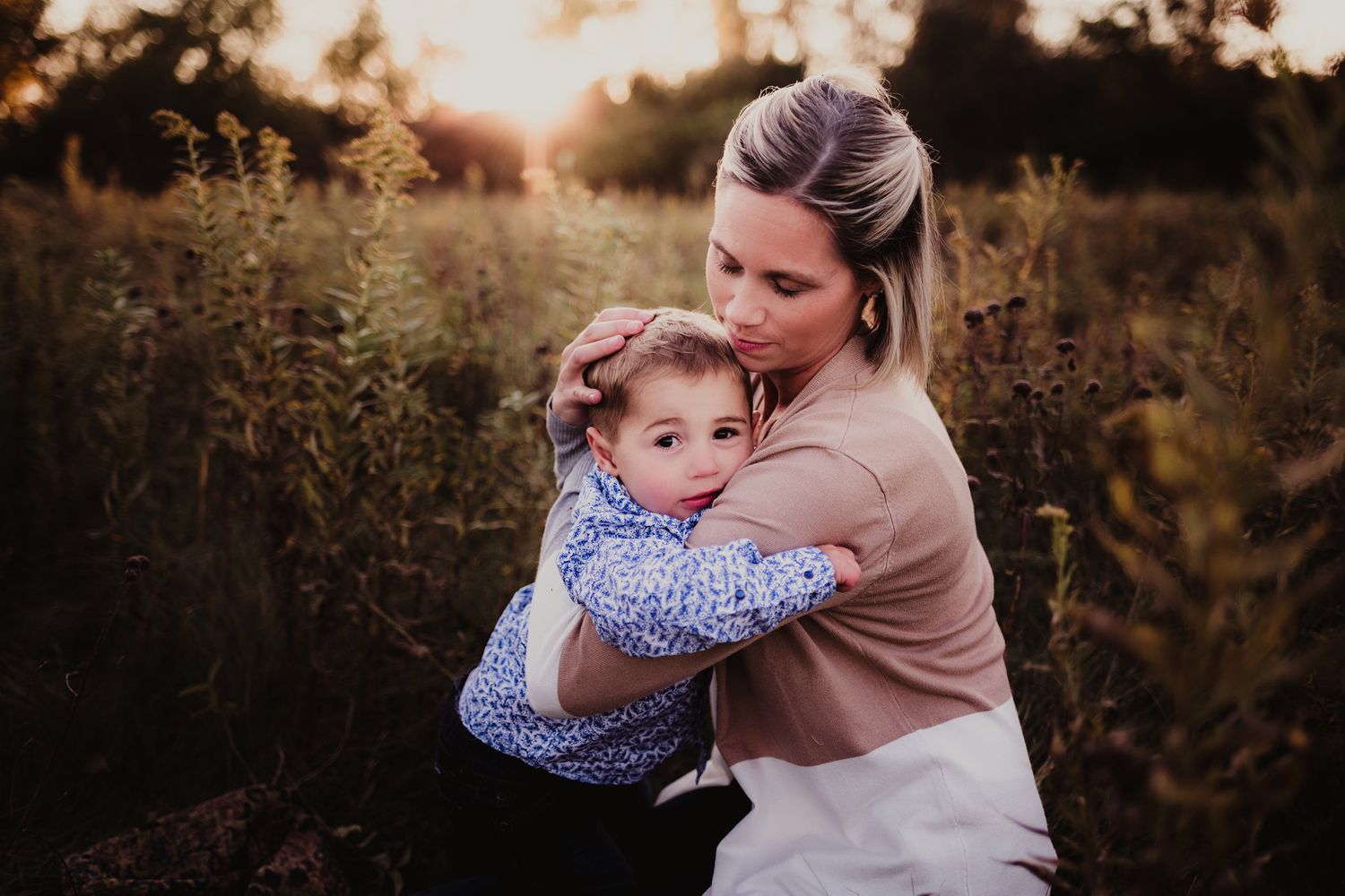 Emotional outdoor portrait of adult hugging child in natural setting at sunset.
