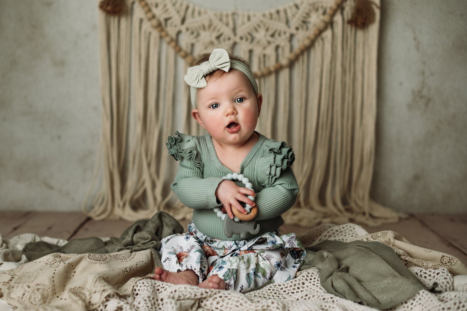 Baby in sage romper makes expressive face while sitting on textured blanket.