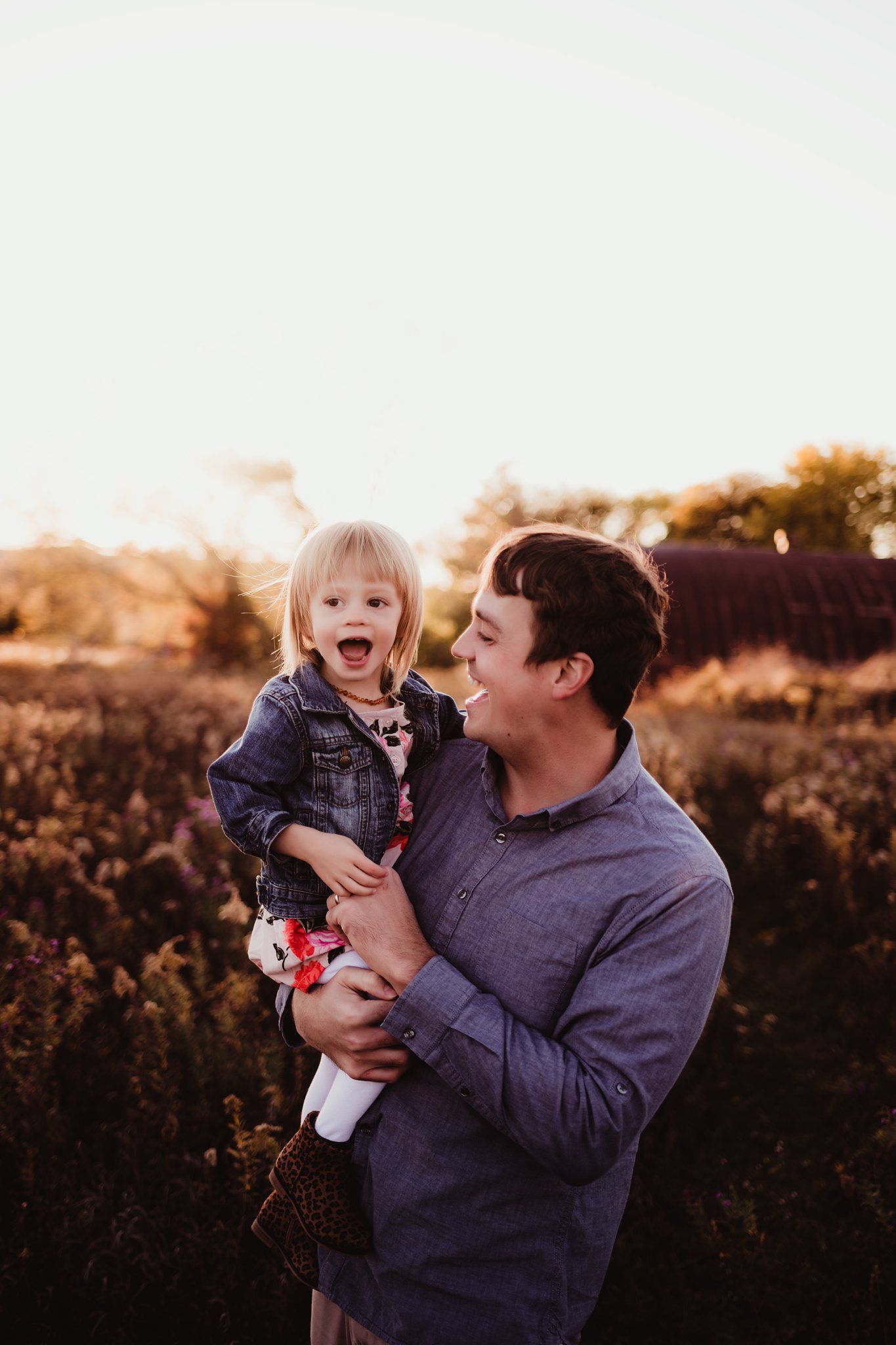 Candid sunset portrait capturing genuine laughter between parent and child outdoors.