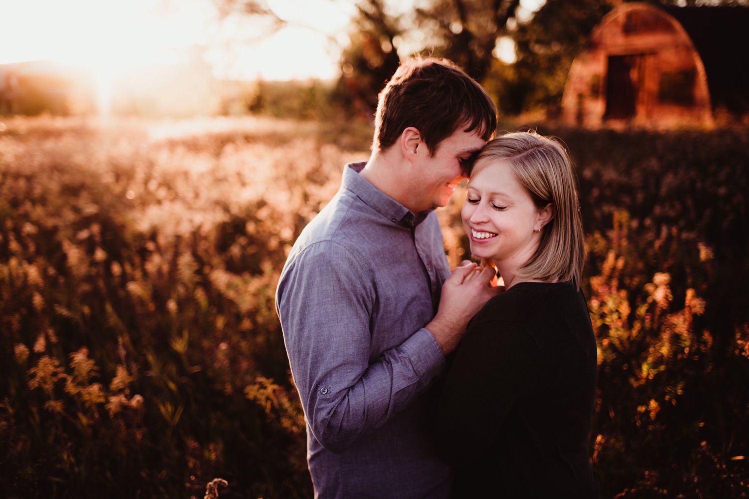 An intimate portrait of a couple in golden sunlight with a rustic barn setting.