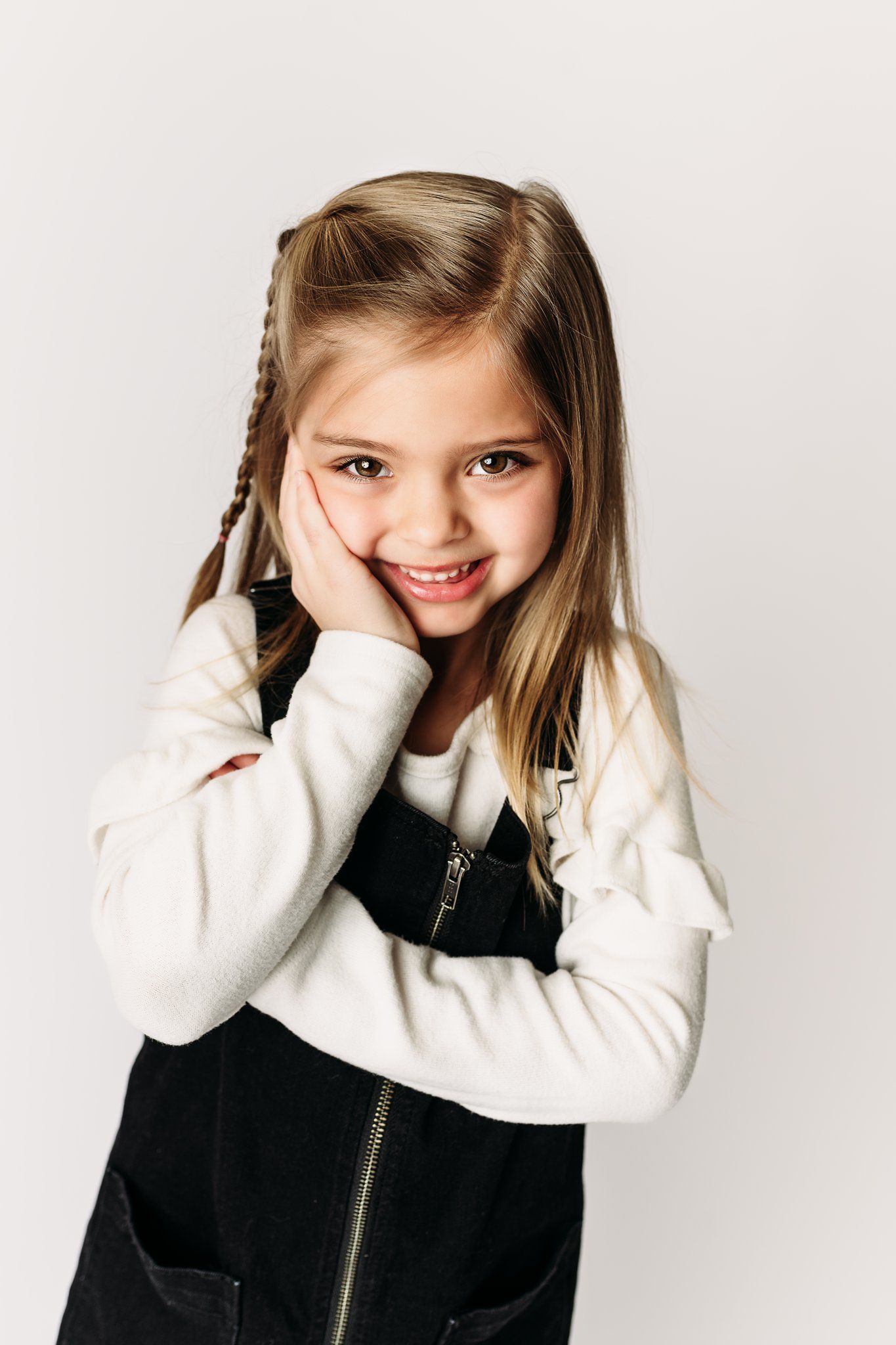 Playful portrait of child in black and white outfit resting head on hand.