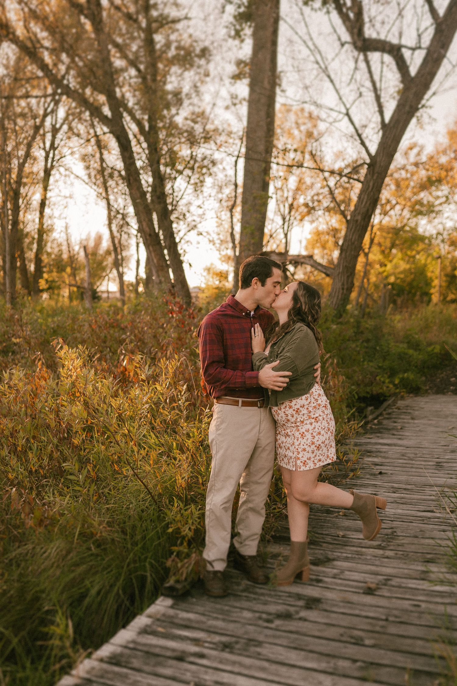 A romantic moment shared between two people on a wooden walkway during golden hour.
