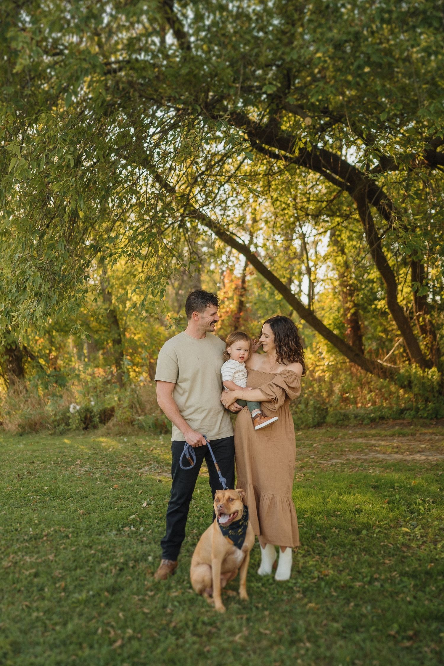 Family portrait in golden autumn setting with a brown dog sitting obediently at their feet.