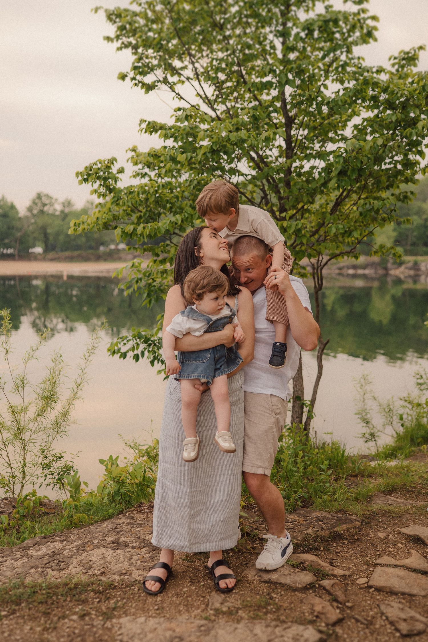 A family sharing an intimate embrace beside a serene lake on a summer evening.