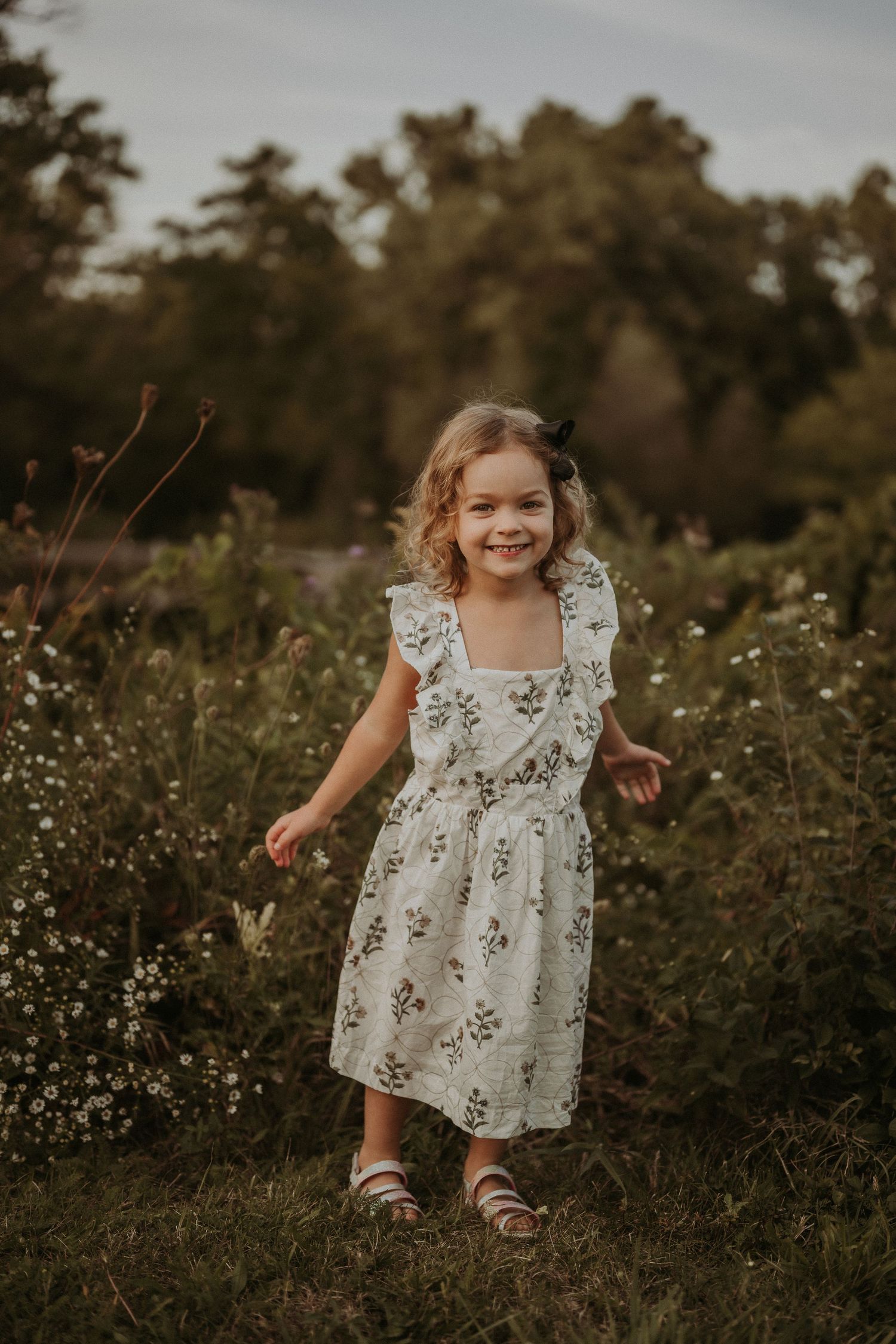 Young child in a floral dress running joyfully through a wildflower meadow at sunset.