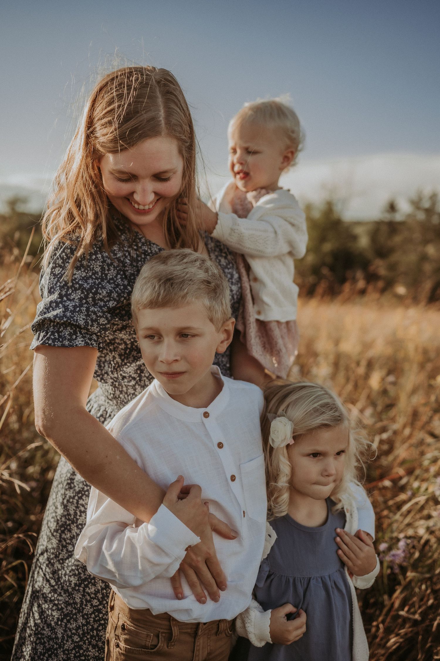 Candid family moment captured in sunlit meadow with natural landscape backdrop.