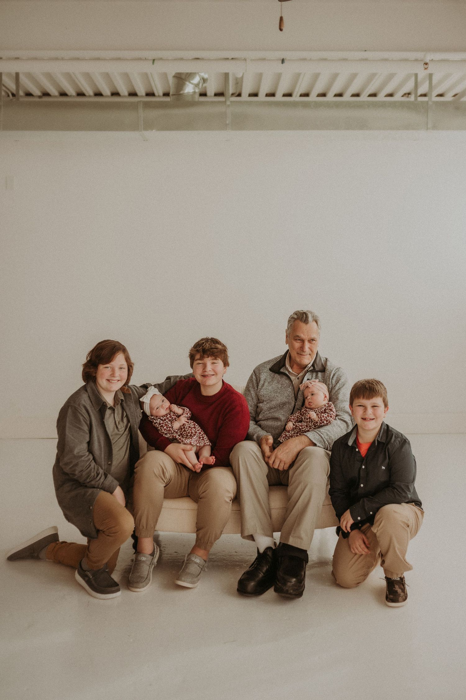 Family portrait of five people seated on beige couch against white studio background.