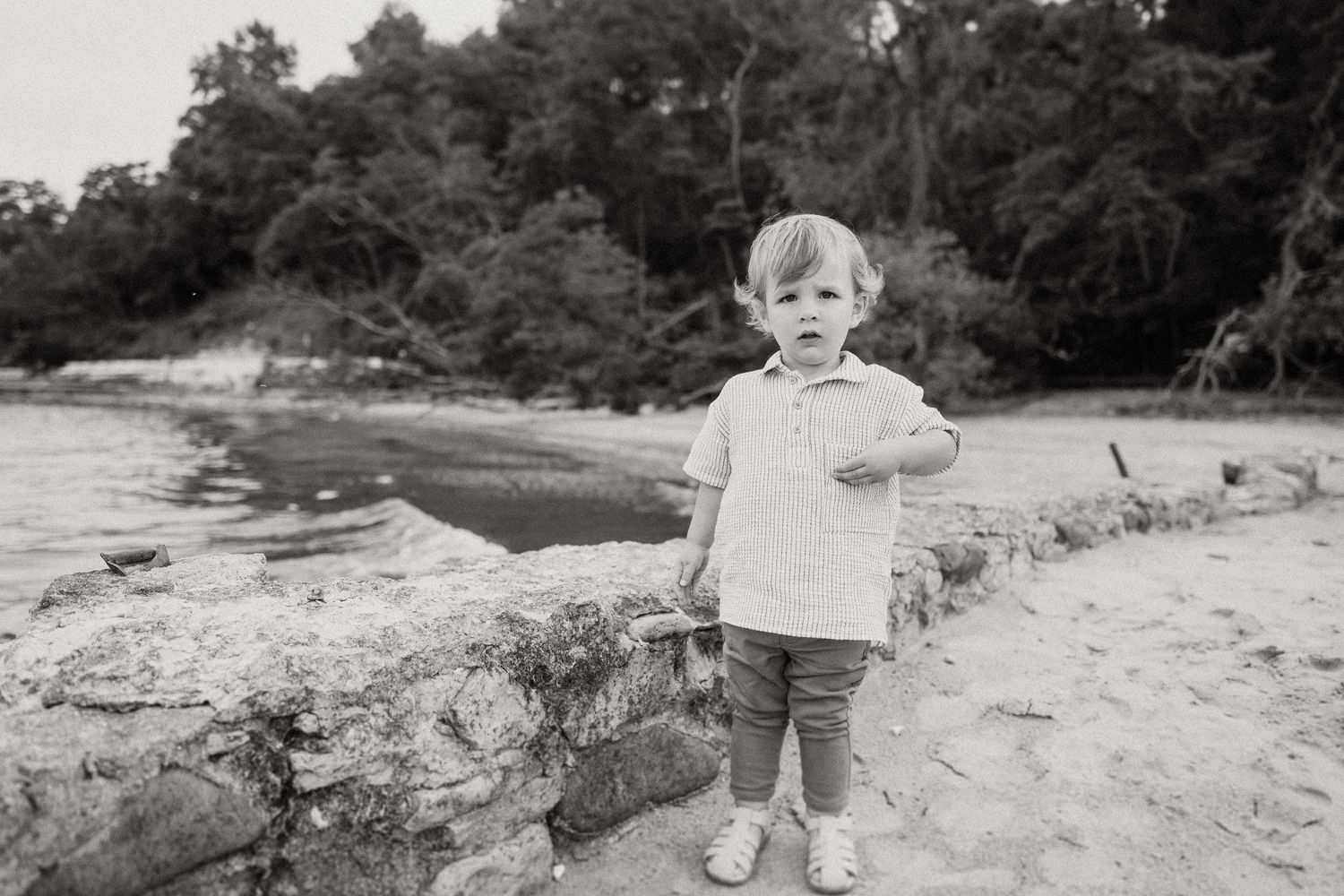 A child stands on a rocky beach shoreline in black and white.
