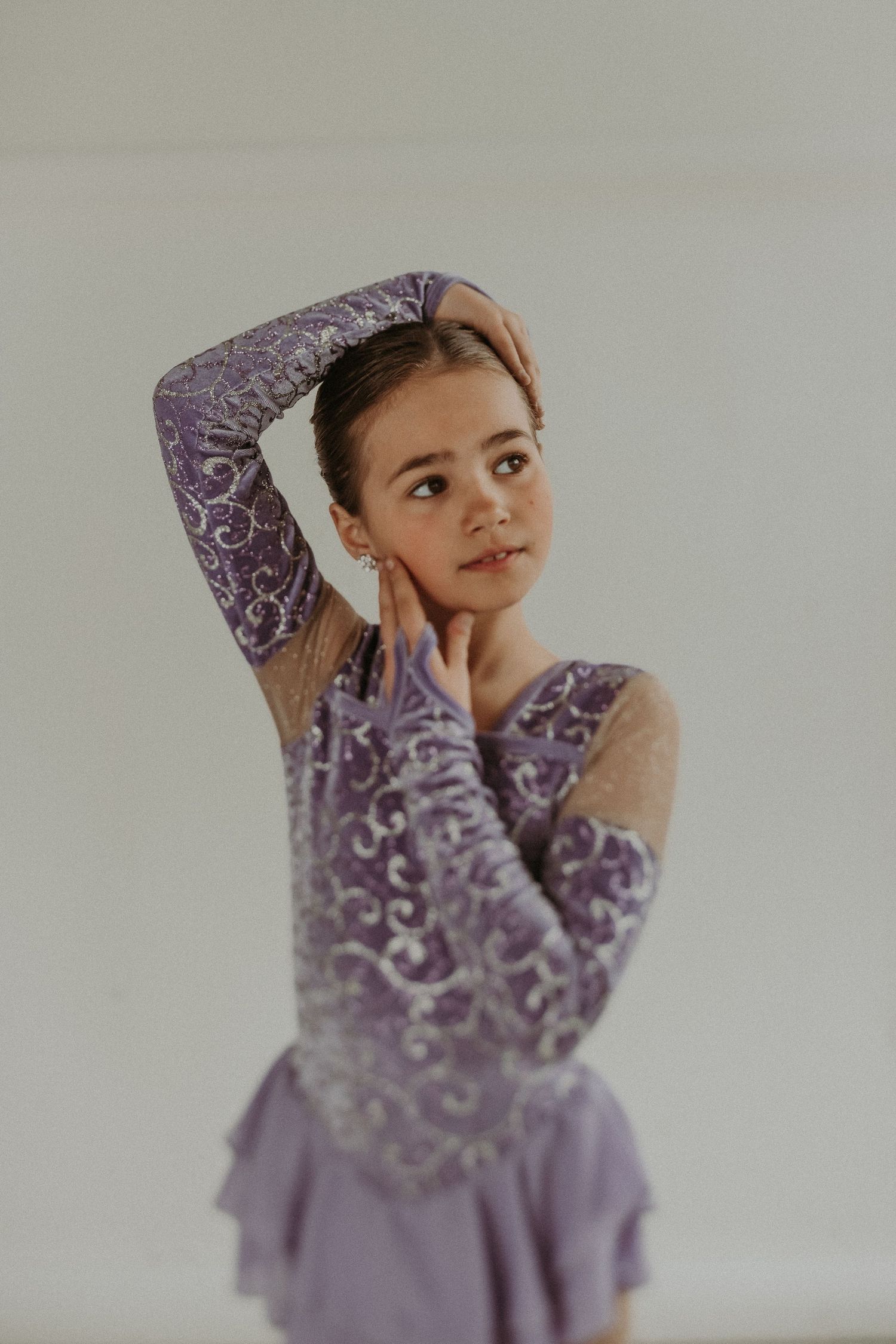 Artistic portrait of figure skater wearing ornate purple costume with sheer sleeves.