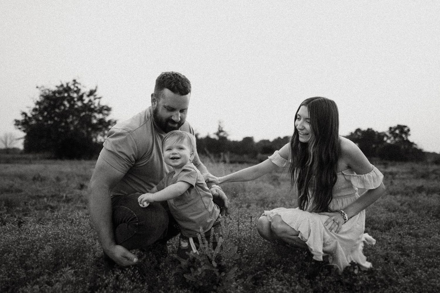 Black and white photo of a playful family moment outdoors in a grassy field.