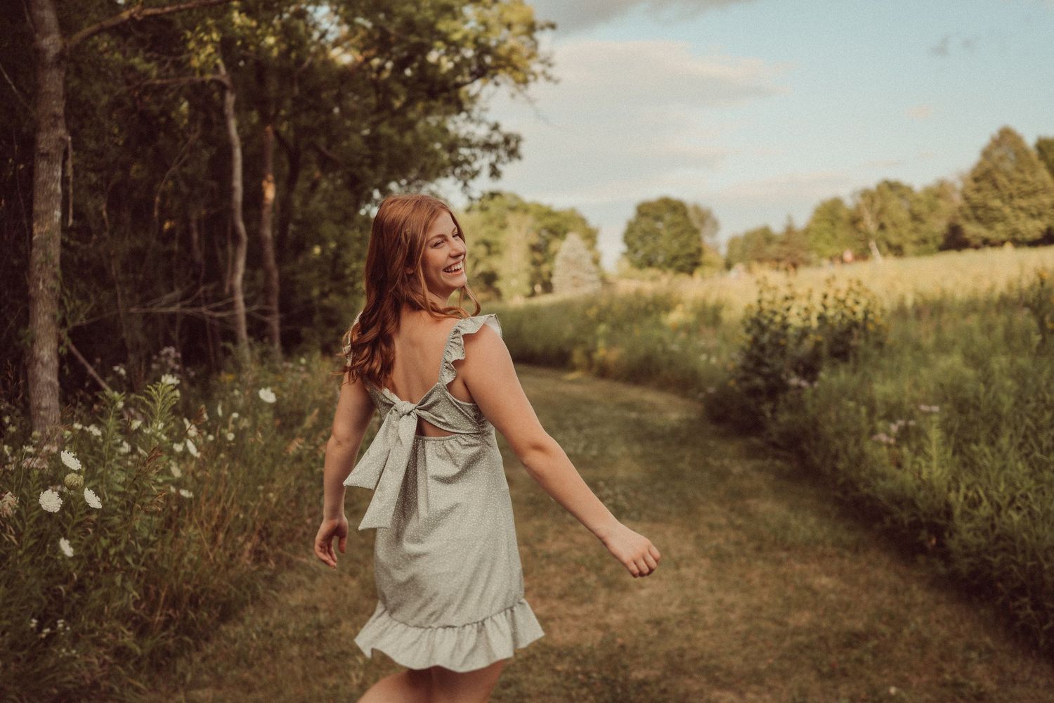 A carefree moment on a summer path as someone in a ruffled dress walks through wildflowers.
