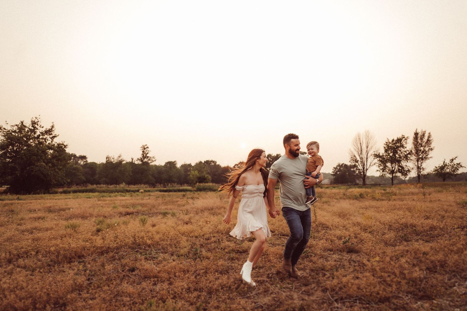Couple running together through a golden field at sunset.