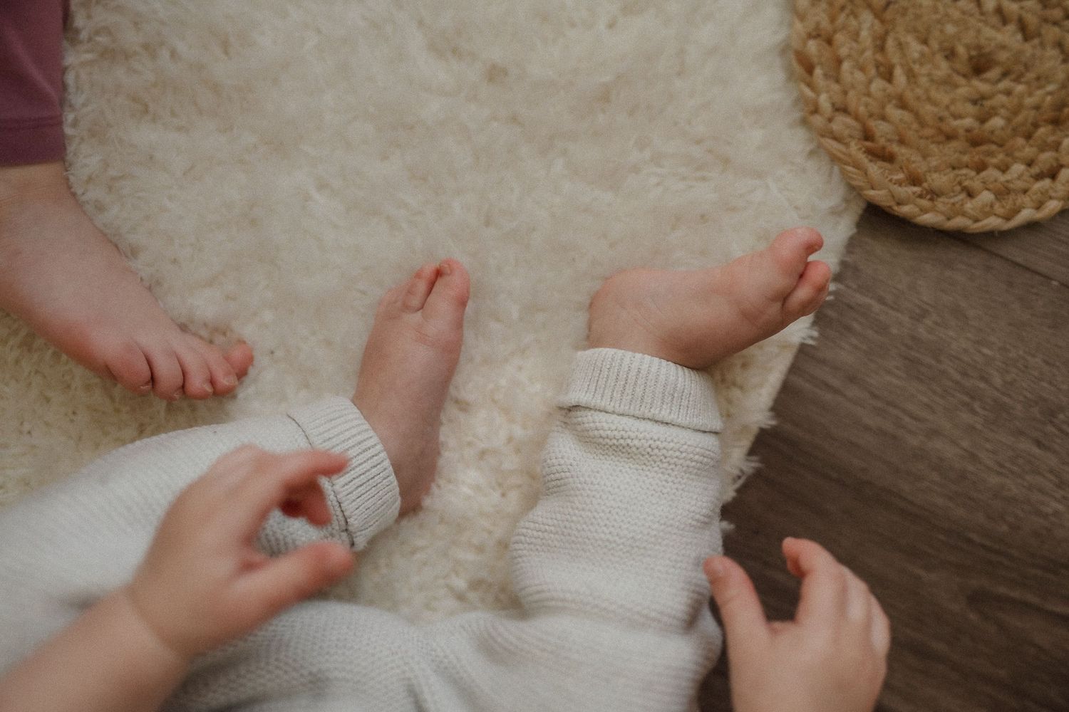Hands adjusting white clothing on a plush carpet with wooden flooring visible.
