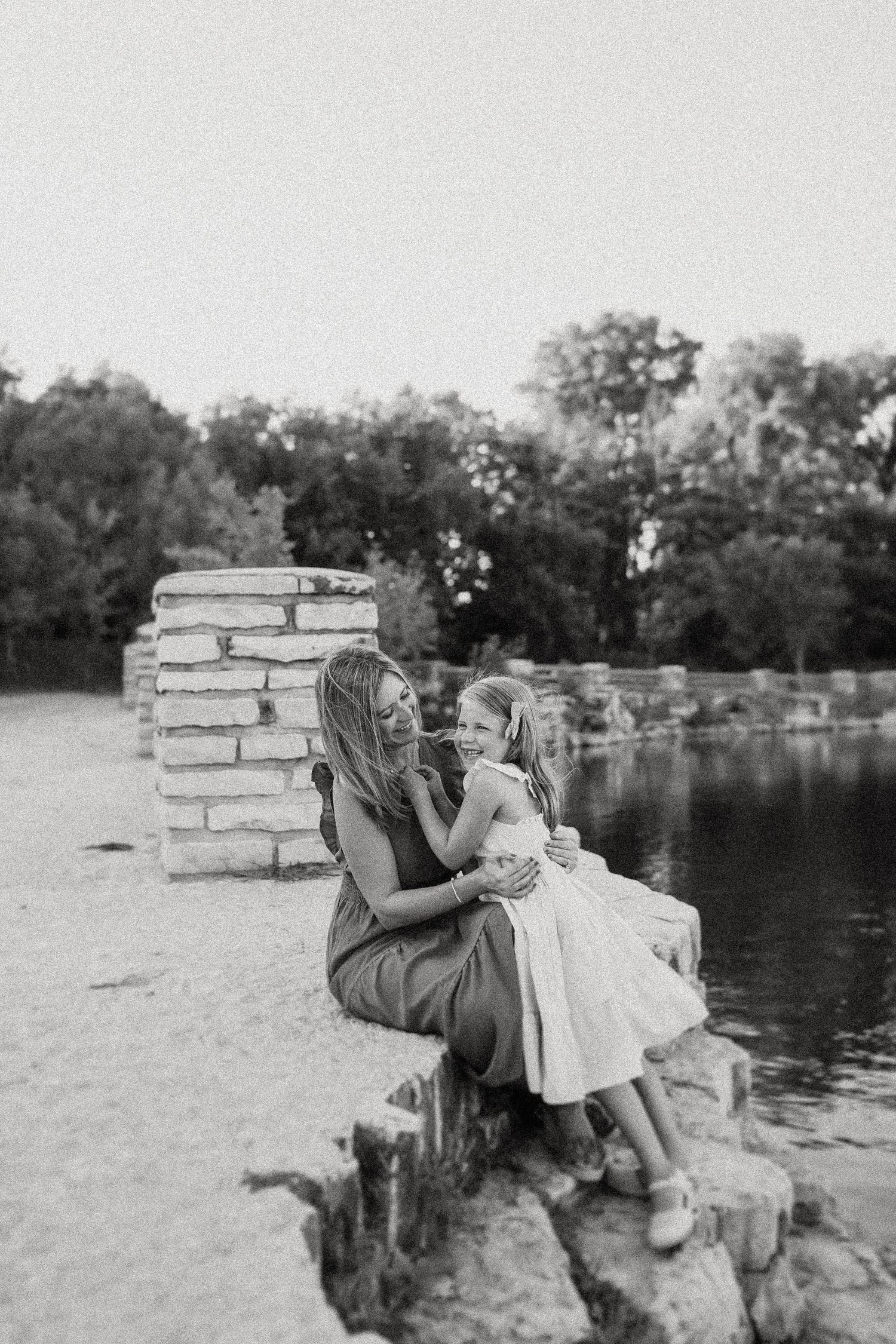 A tender moment captured in black and white by a pond with stone walls in the background.