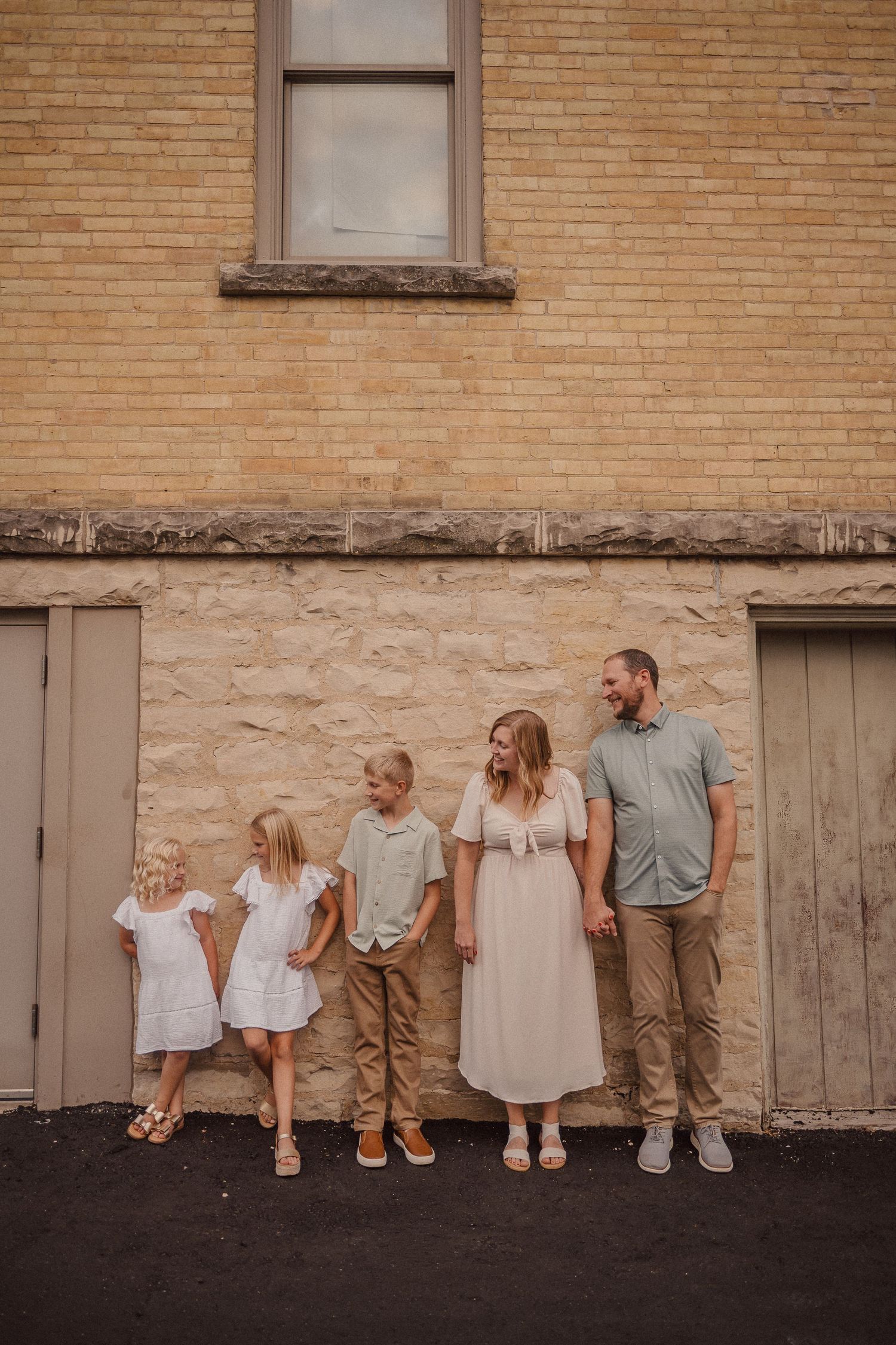 Family members line up against tan brick wall wearing coordinated neutral outfits.