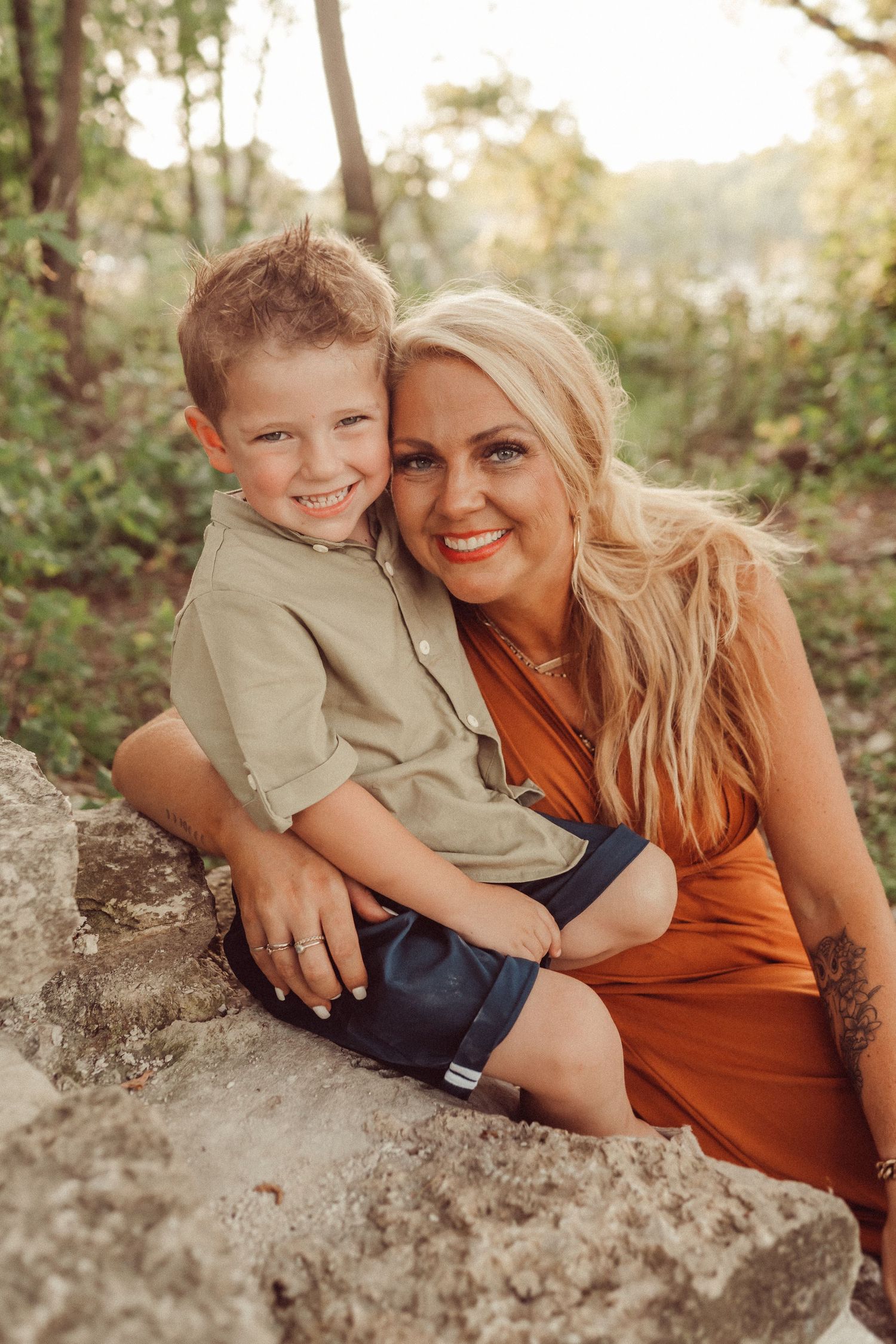 Family portrait on stone ledge surrounded by lush greenery in warm evening light.